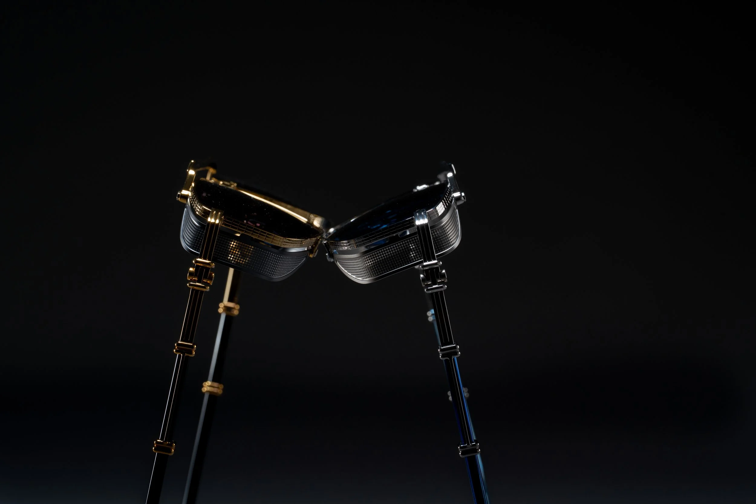 Close-up of two pairs of sunglasses, one gold and one silver, facing each other against a dark background.