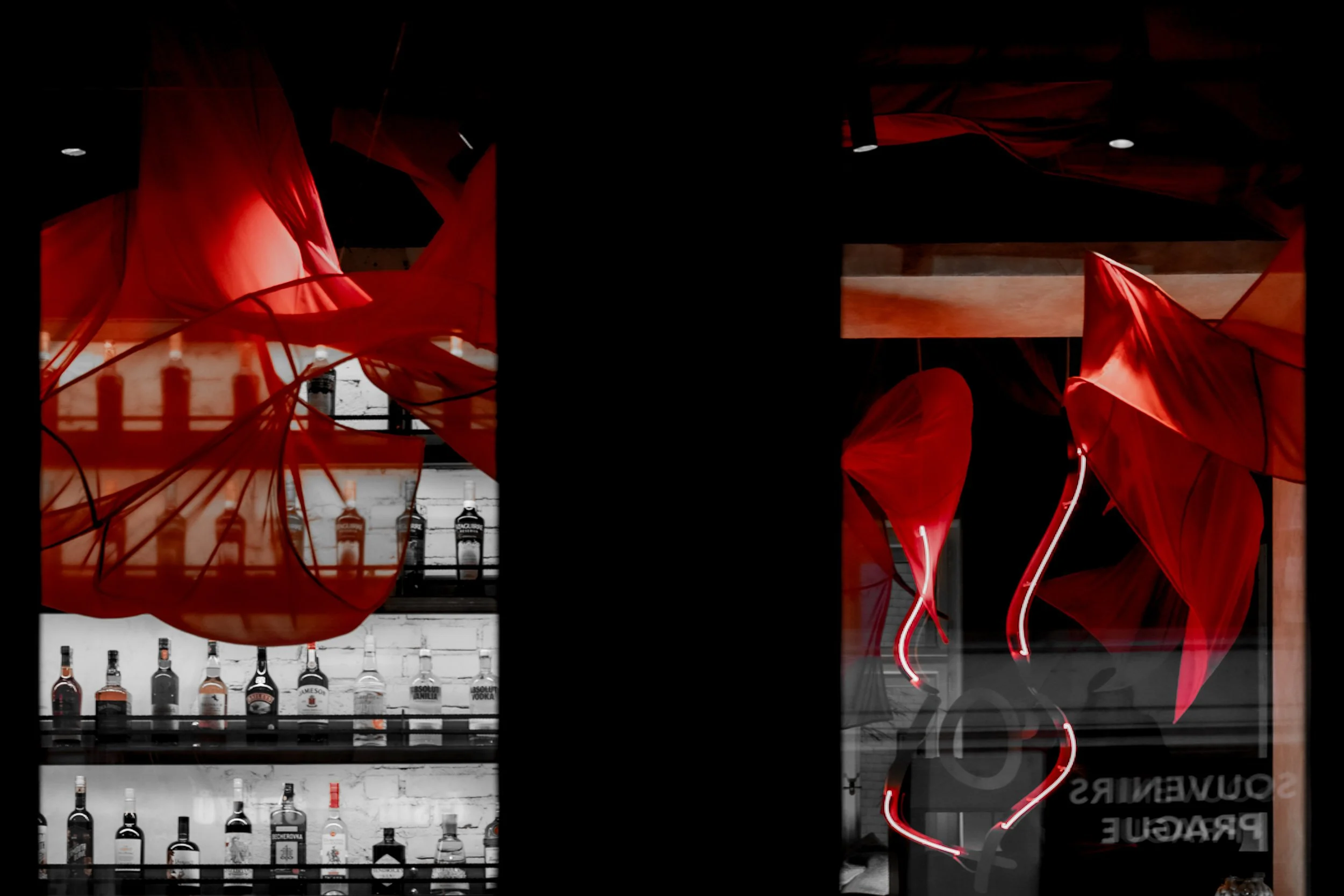 Bar interior with illuminated liquor bottles on shelves, surrounded by red fabric and decorative lighting elements.