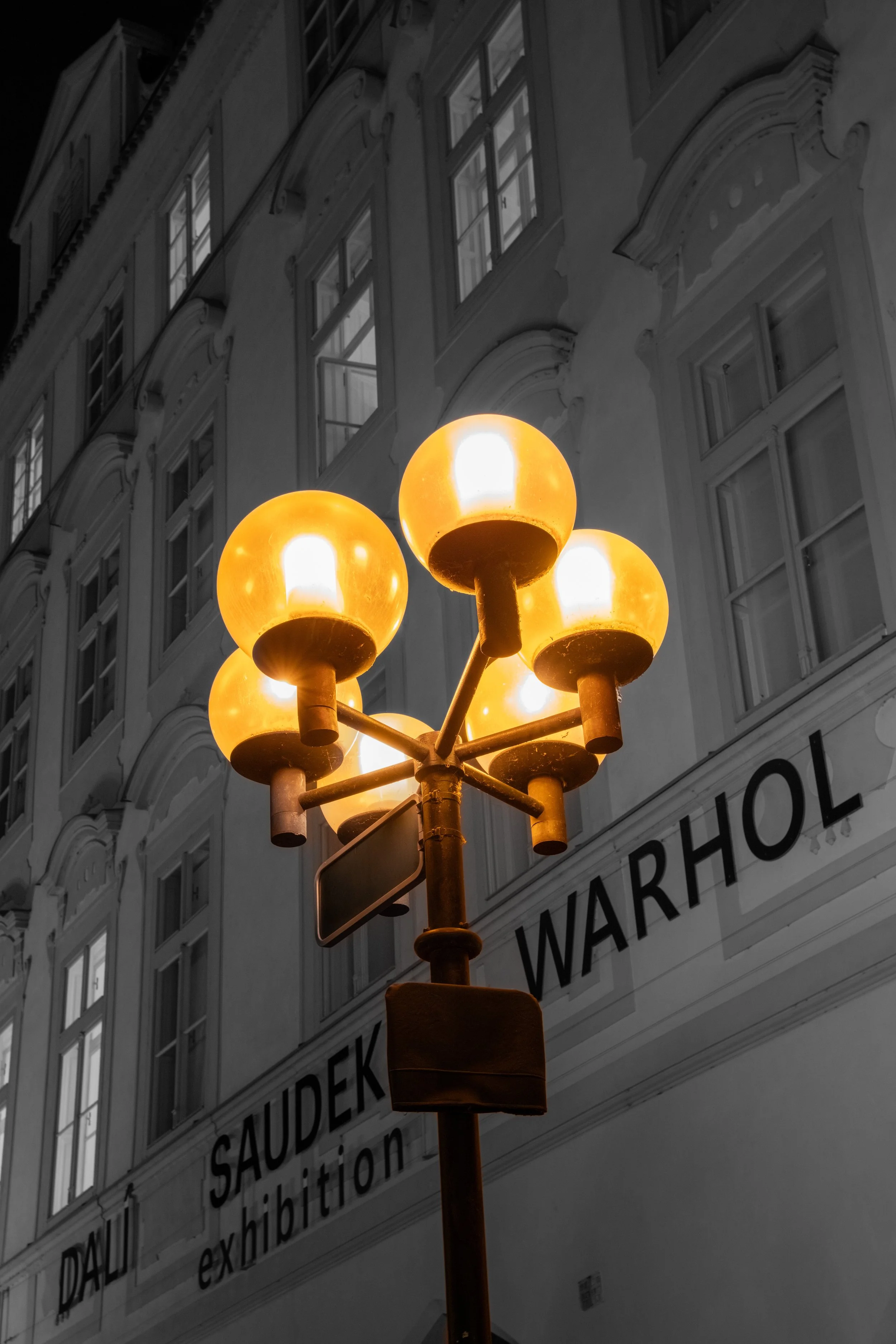 A vintage street lamp with five bright yellow globes against a black and white building background.