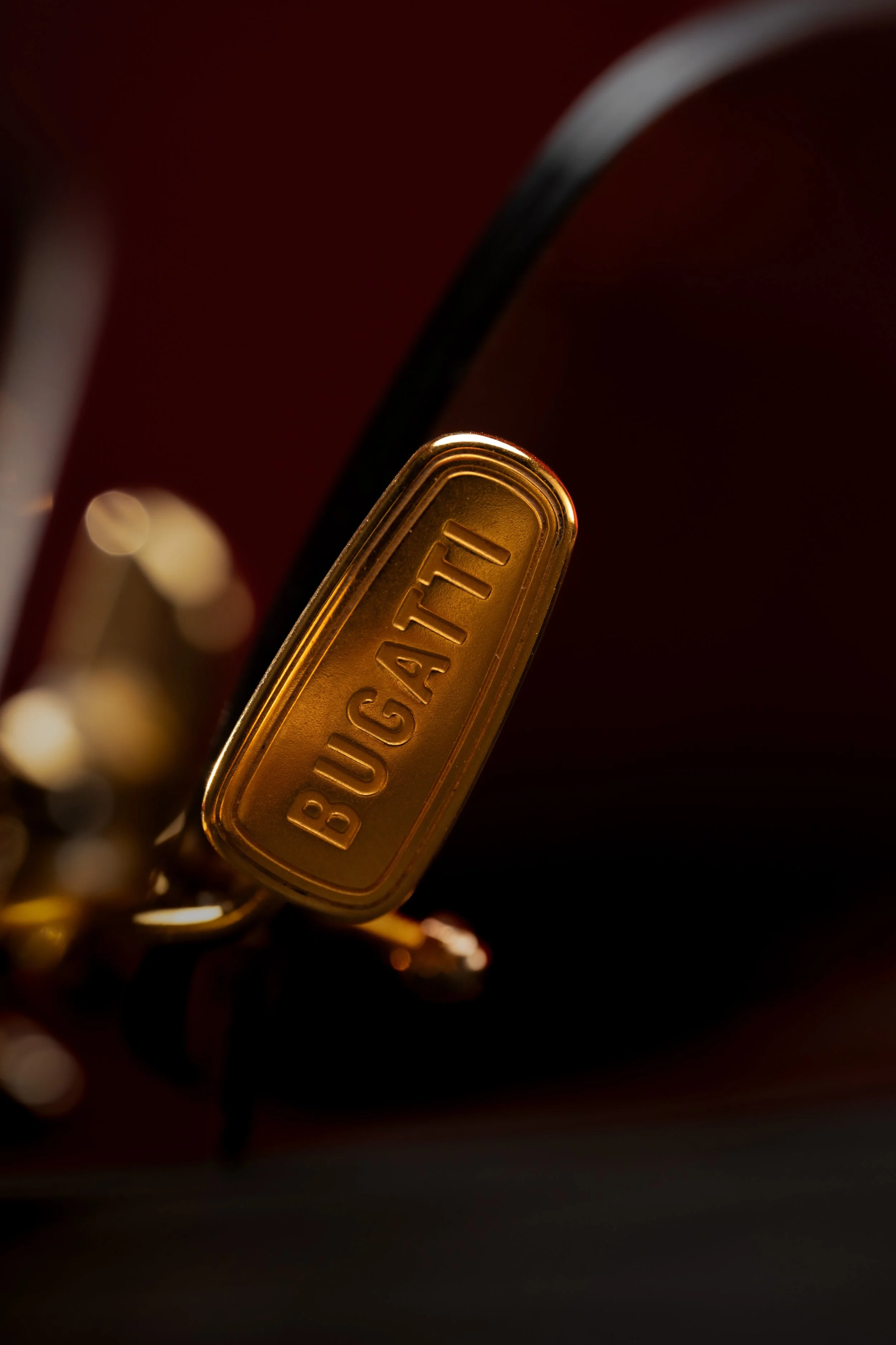 Close-up of a gold keychain with the word 'BUGATTI' engraved, attached to a dark background.