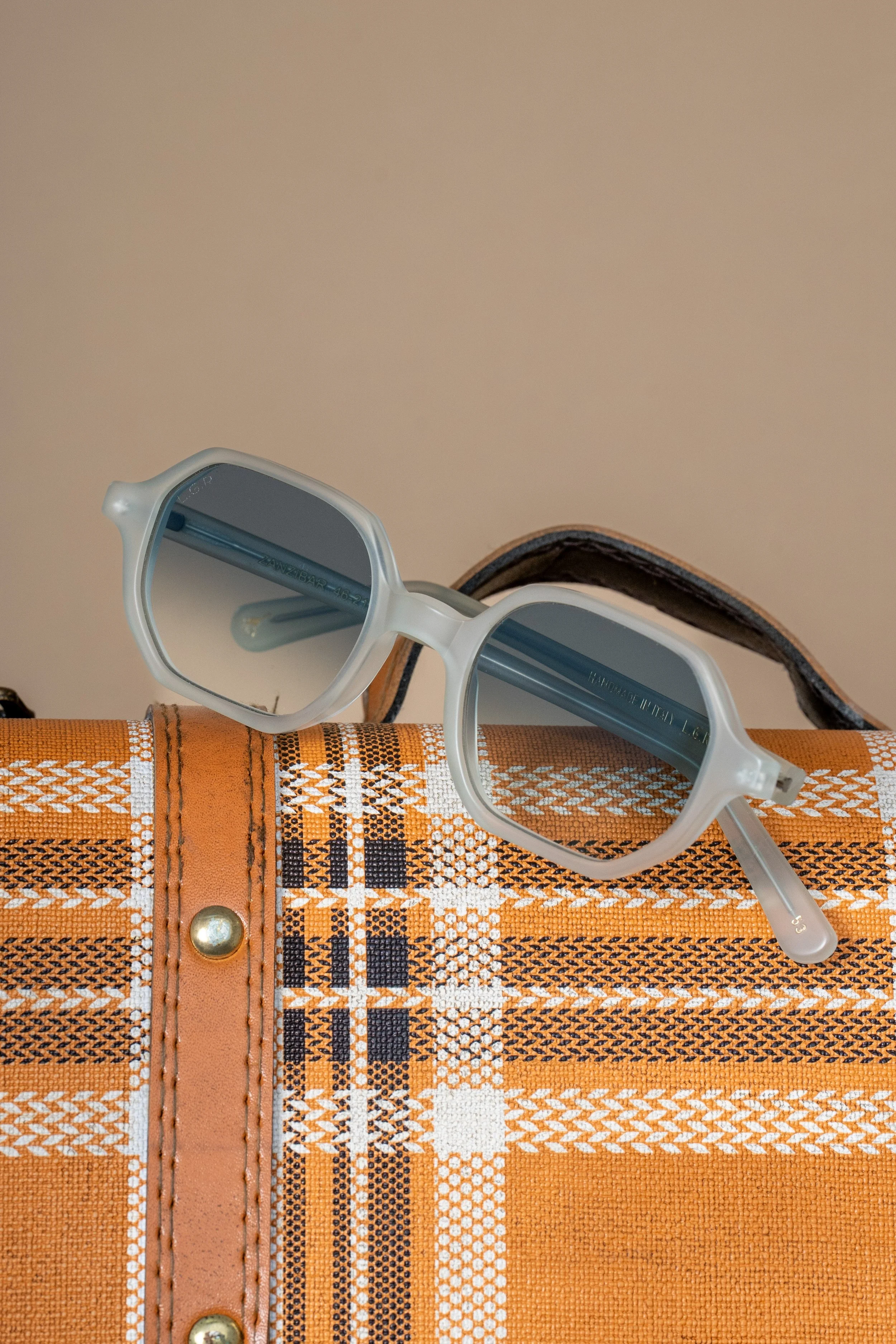 A pair of white sunglasses resting on an orange and white plaid-patterned bag.