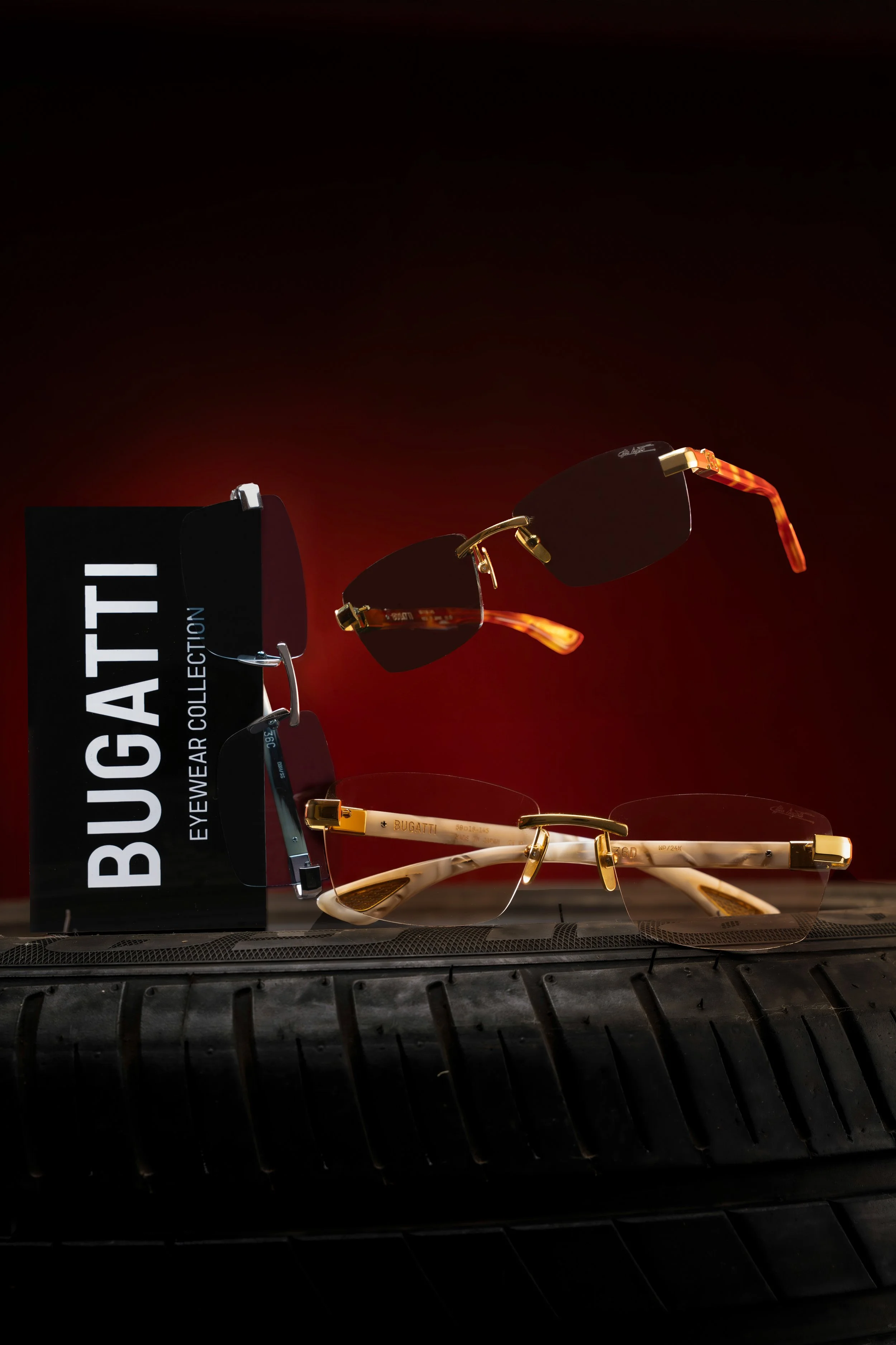A display of three pairs of designer sunglasses, with a sign labeled 'BUGATTI EYEWEAR COLLECTION,' placed on a car tire. The background is dark with a red gradient.