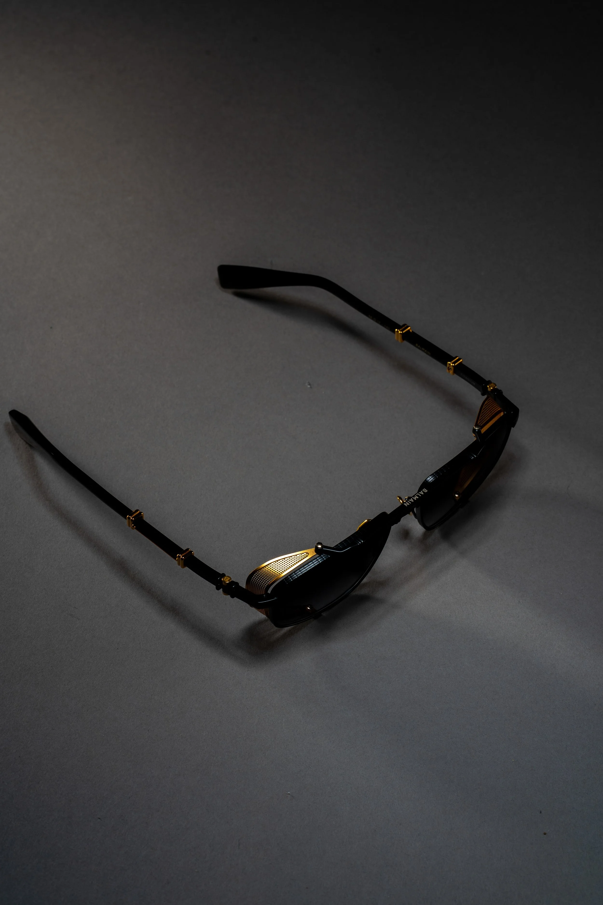 A pair of black sunglasses with gold accents resting on a gray surface.