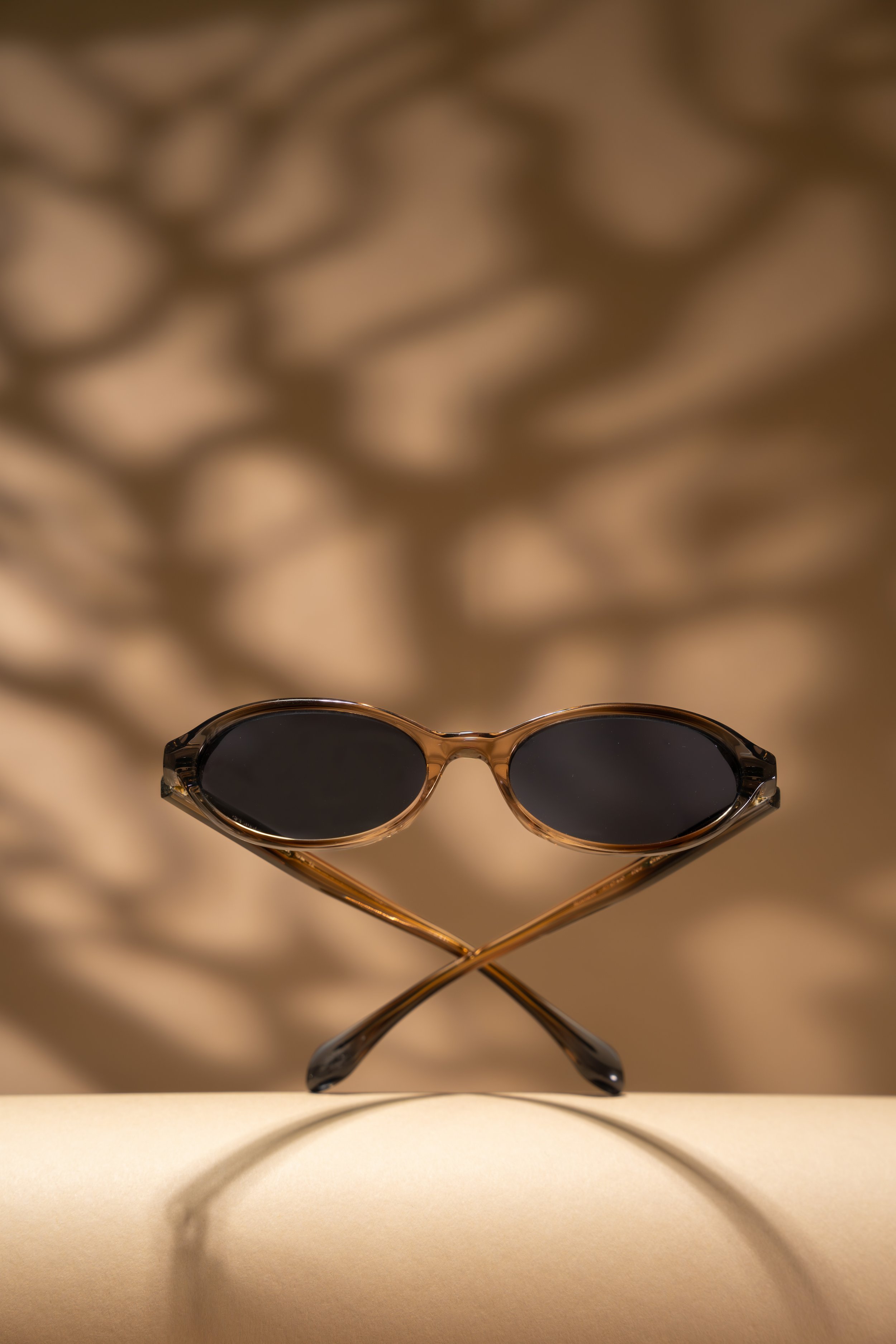 A pair of brown sunglasses with black lenses balanced on the tip of a beige surface, casting a shadow and reflecting light.