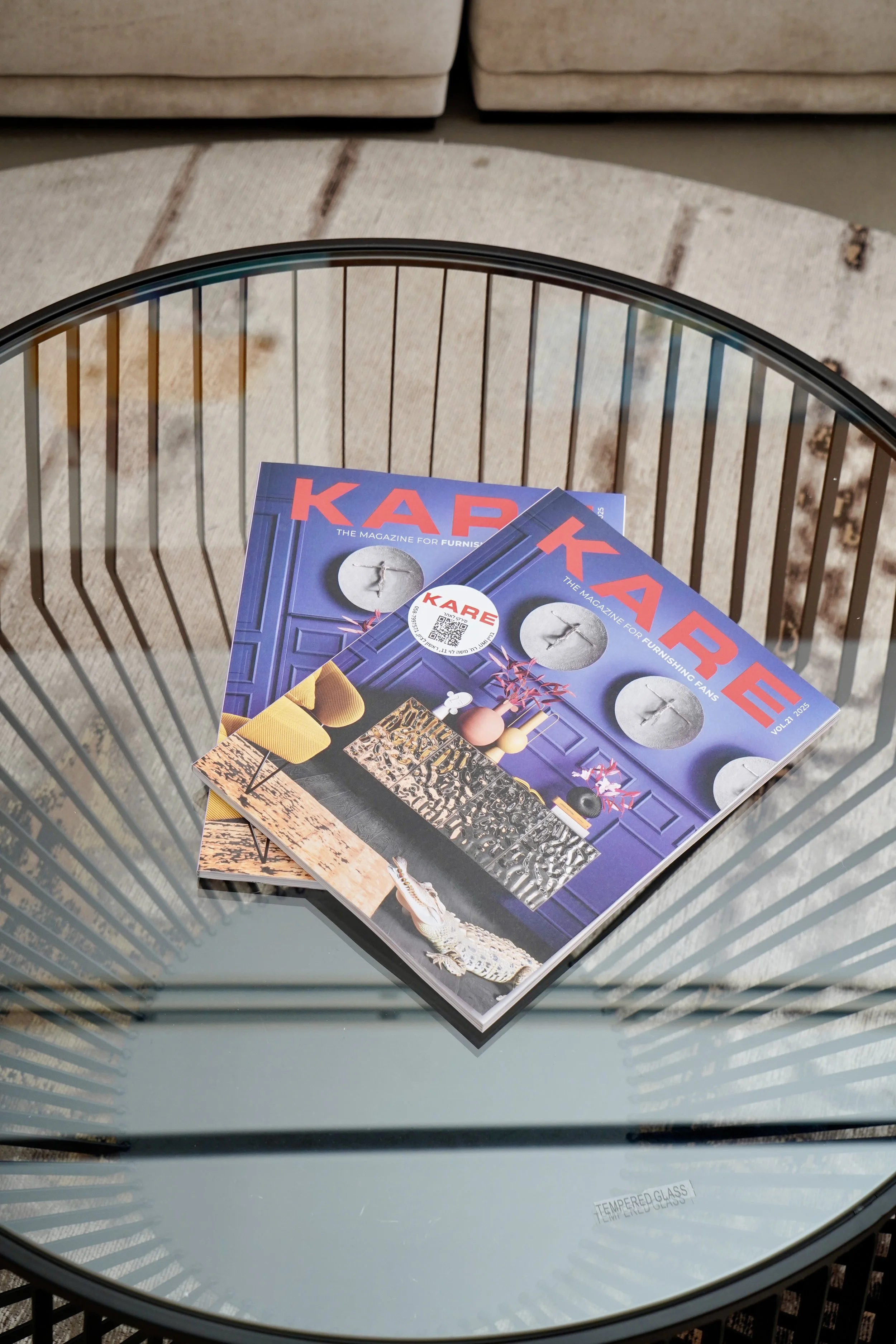Two copies of Kare magazine on a glass coffee table with a wire frame, in a room with a beige carpet and a beige sofa in the background.