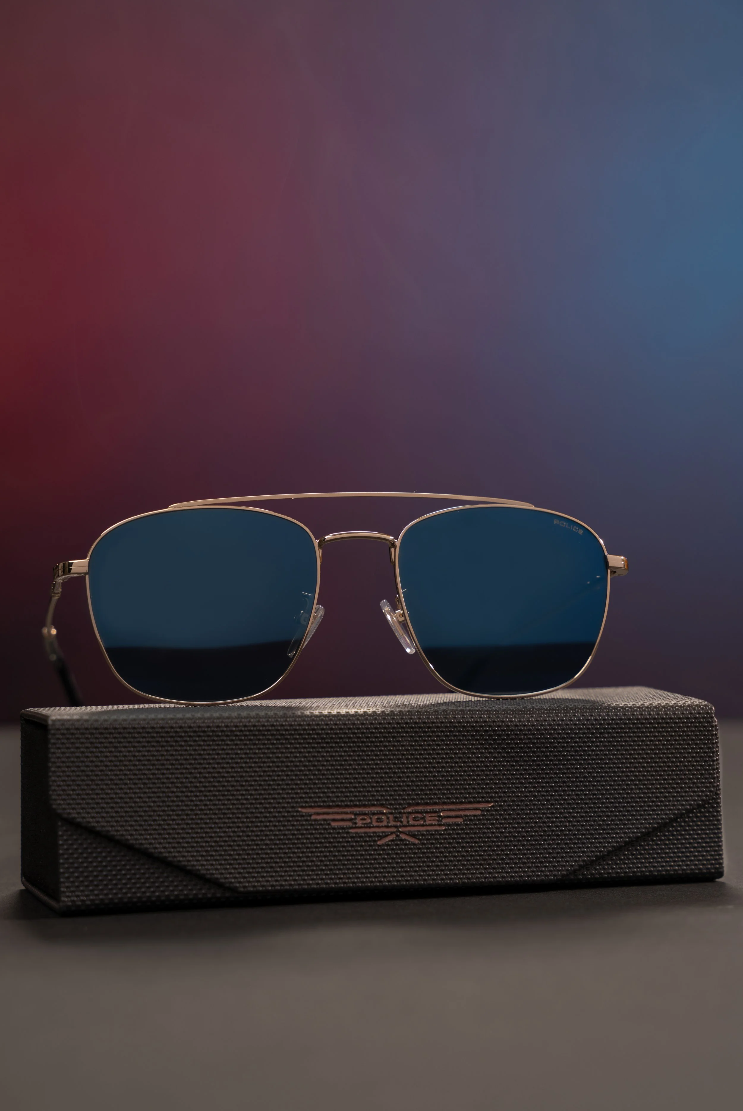 Pair of sunglasses with blue lenses on a black branded case against a gradient background.