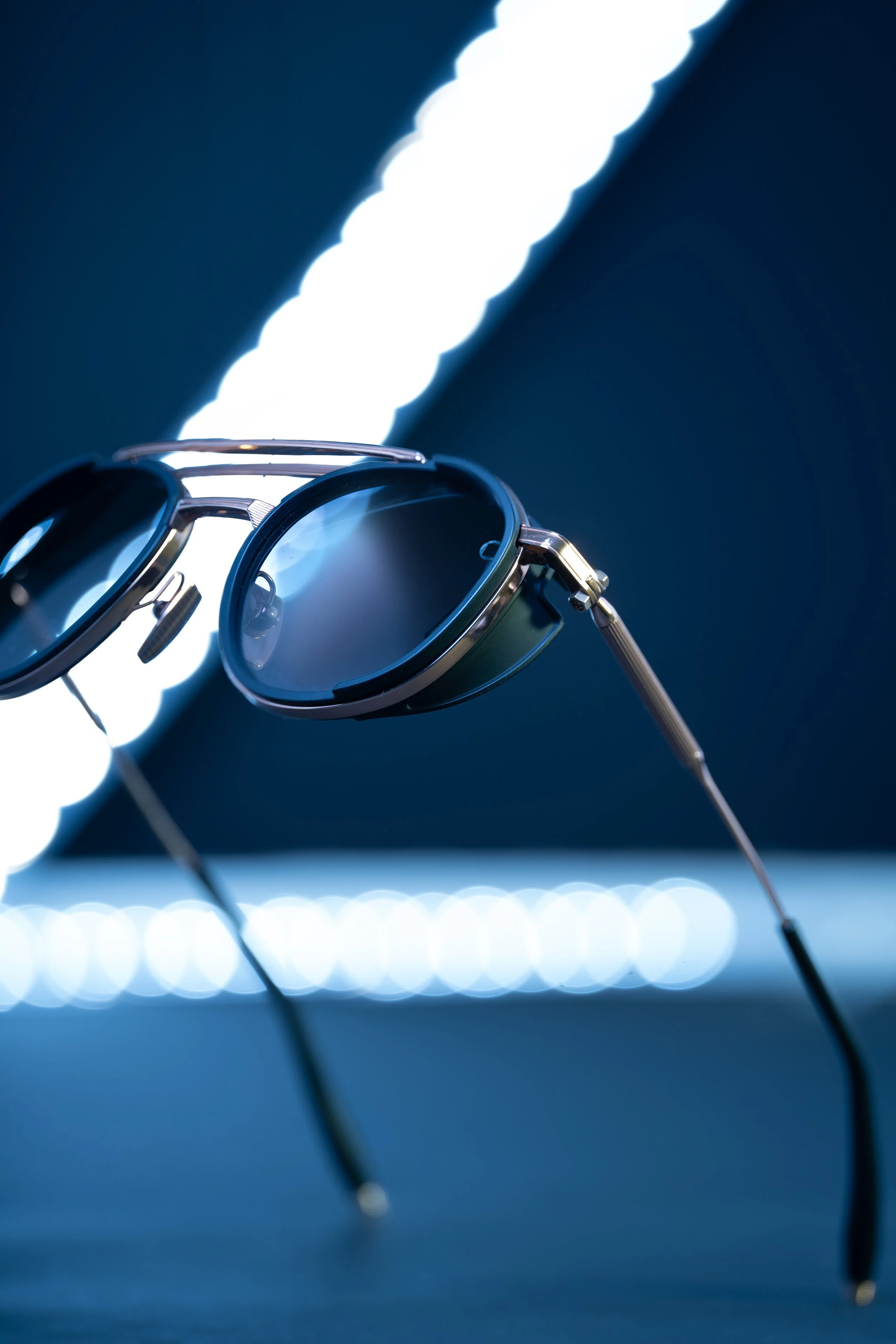 Close-up of vintage sunglasses with dark lenses against a blue background with bright light streaks.