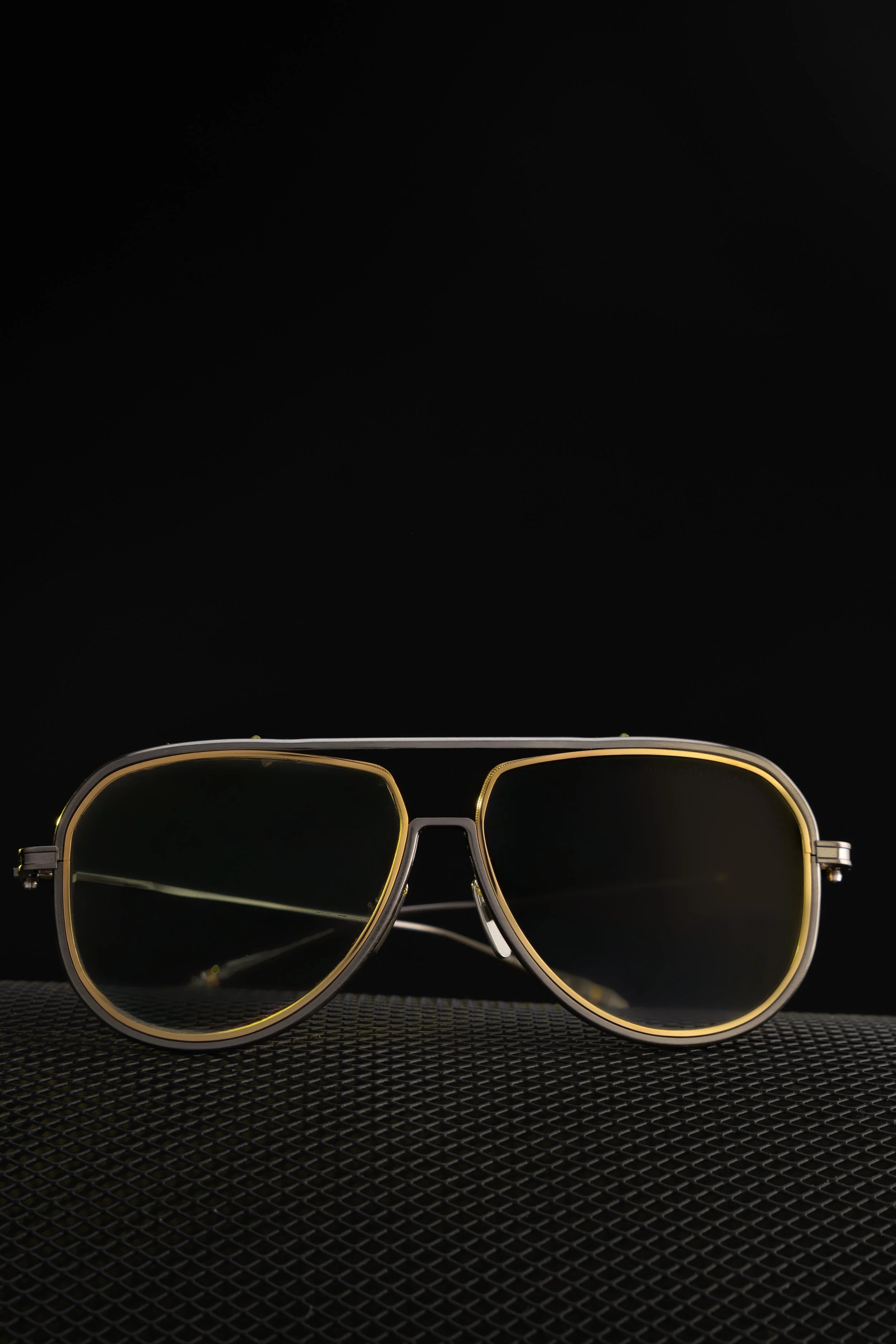 A pair of yellow-tinted sunglasses with a metal frame on a textured dark surface, against a plain black background.