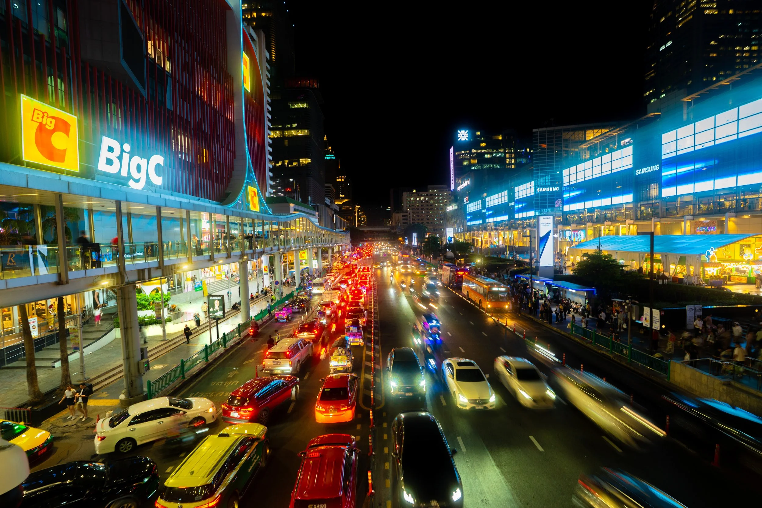 Night scene of busy city street with cars, neon signs, and illuminated buildings.