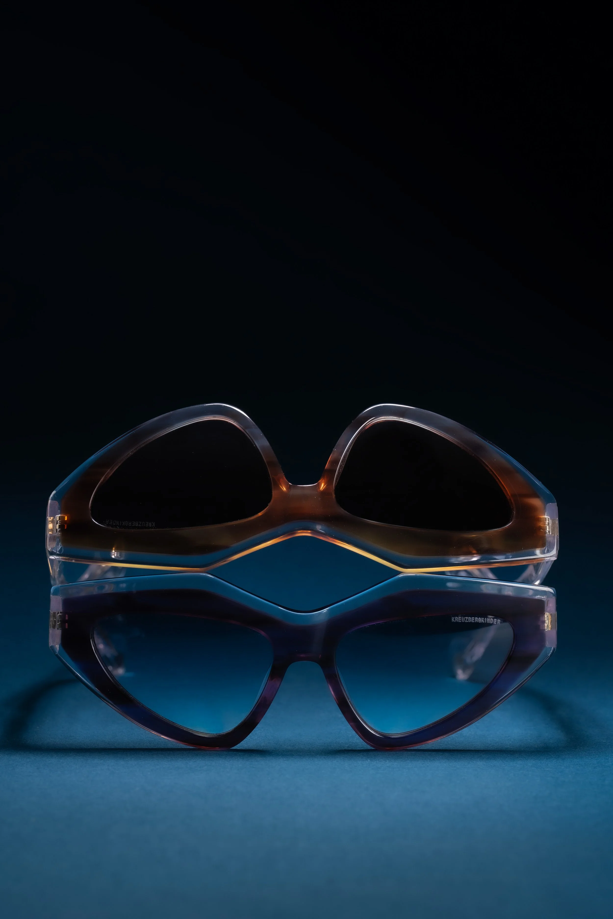 A pair of sunglasses with tinted lenses, reflected on a surface, against a dark background.