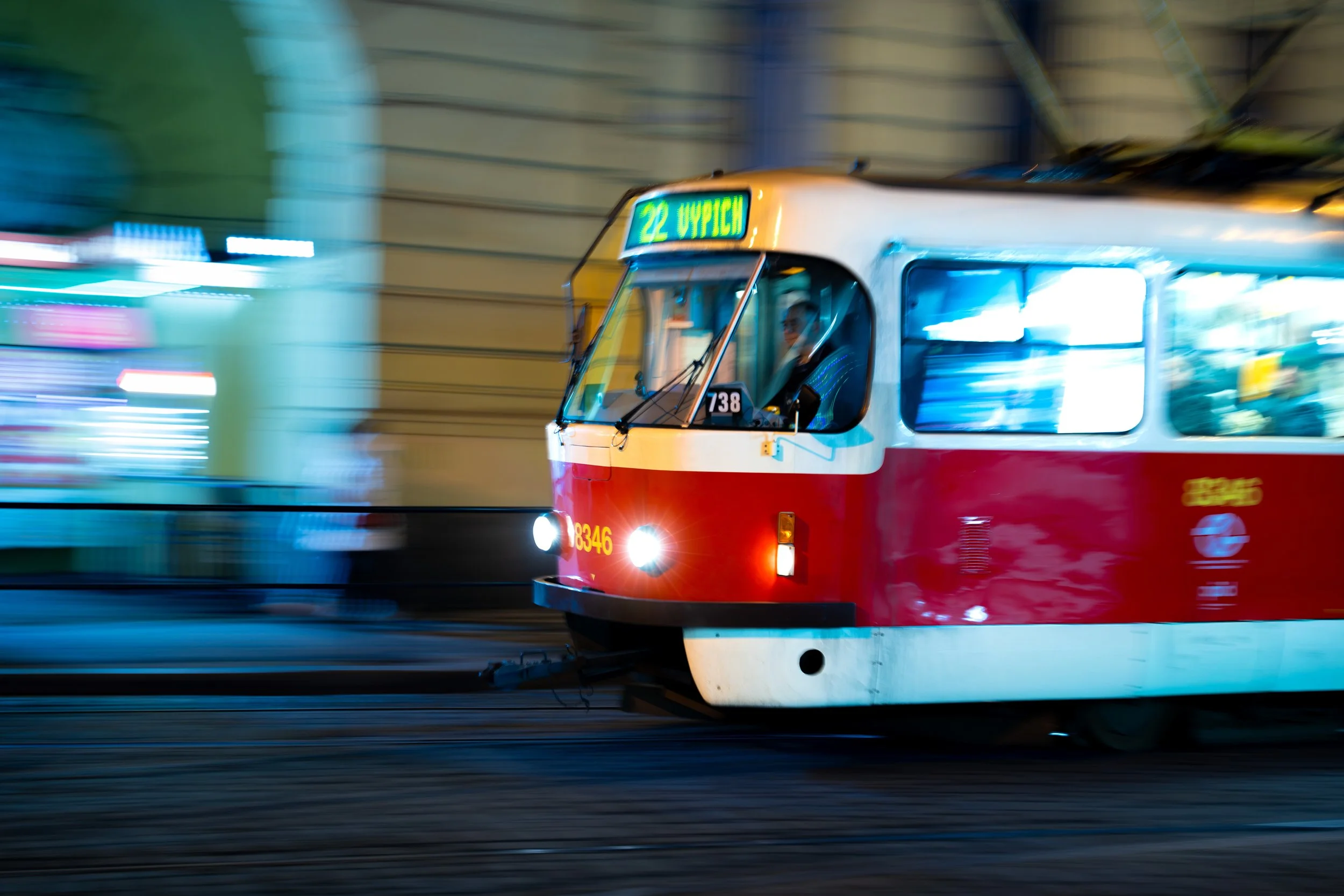 A red and white tram moving quickly through a tunnel at night with bright city lights in the background.