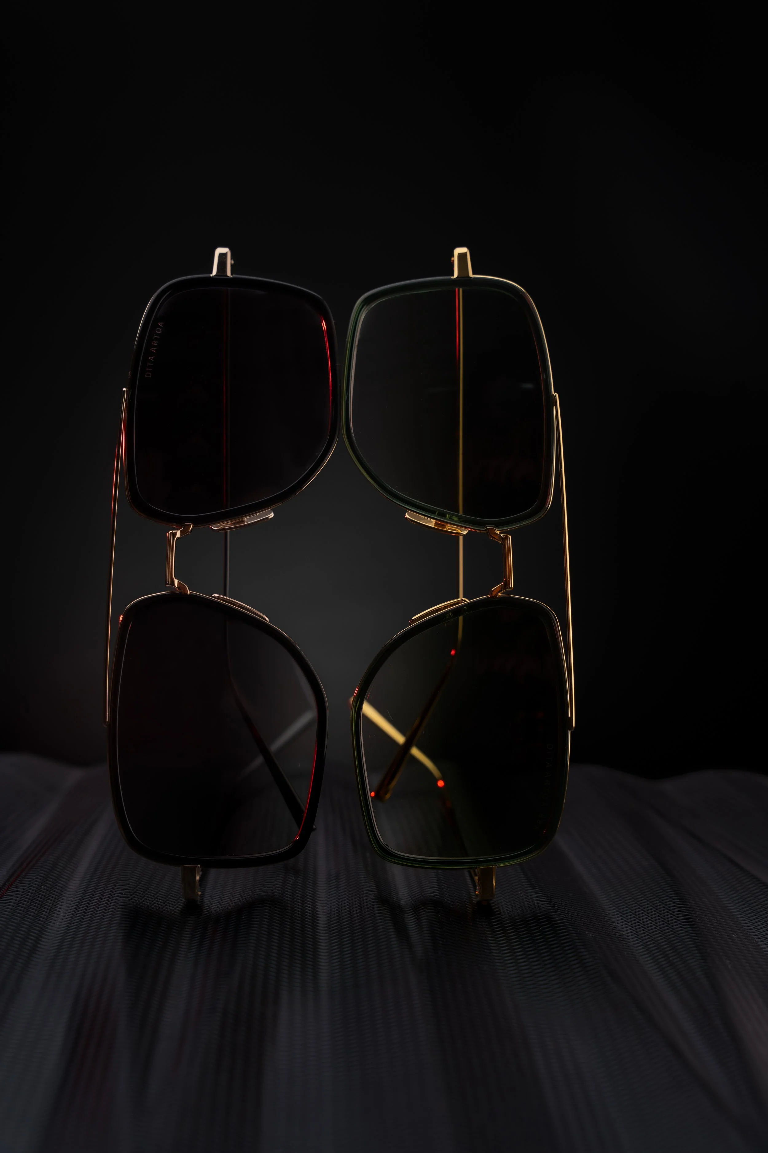 A pair of black sunglasses with gold frames and dark lenses, displayed in a vertical arrangement against a black background.