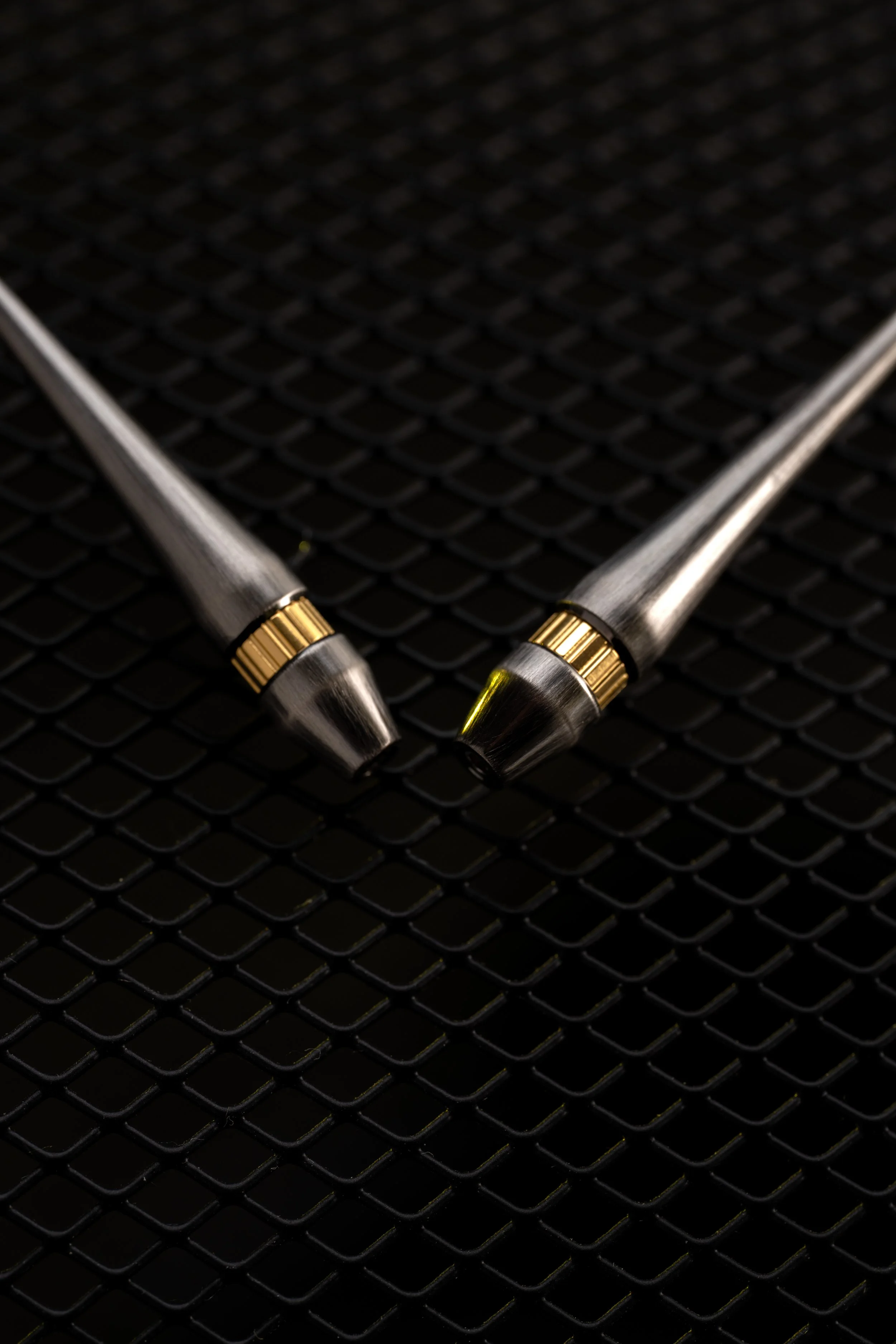 Two styluses with metallic bodies and gold-colored accents on a black textured surface.