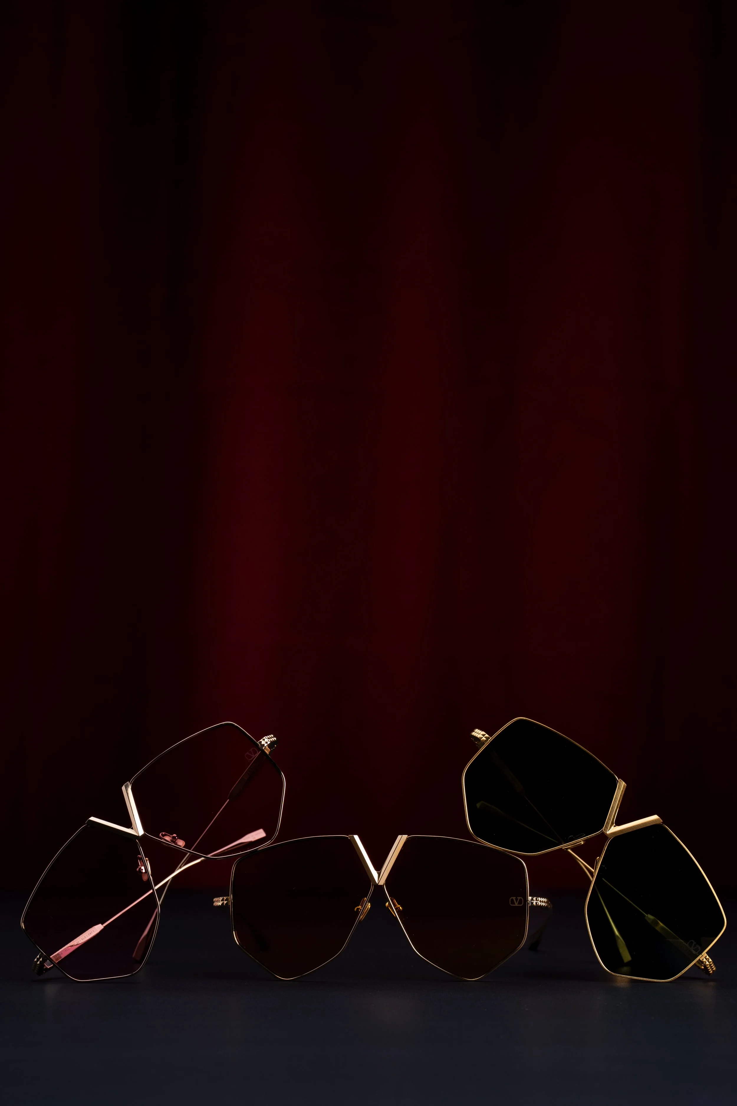 Three pairs of sunglasses with dark lenses and gold frames arranged on a dark surface, with a dark background.