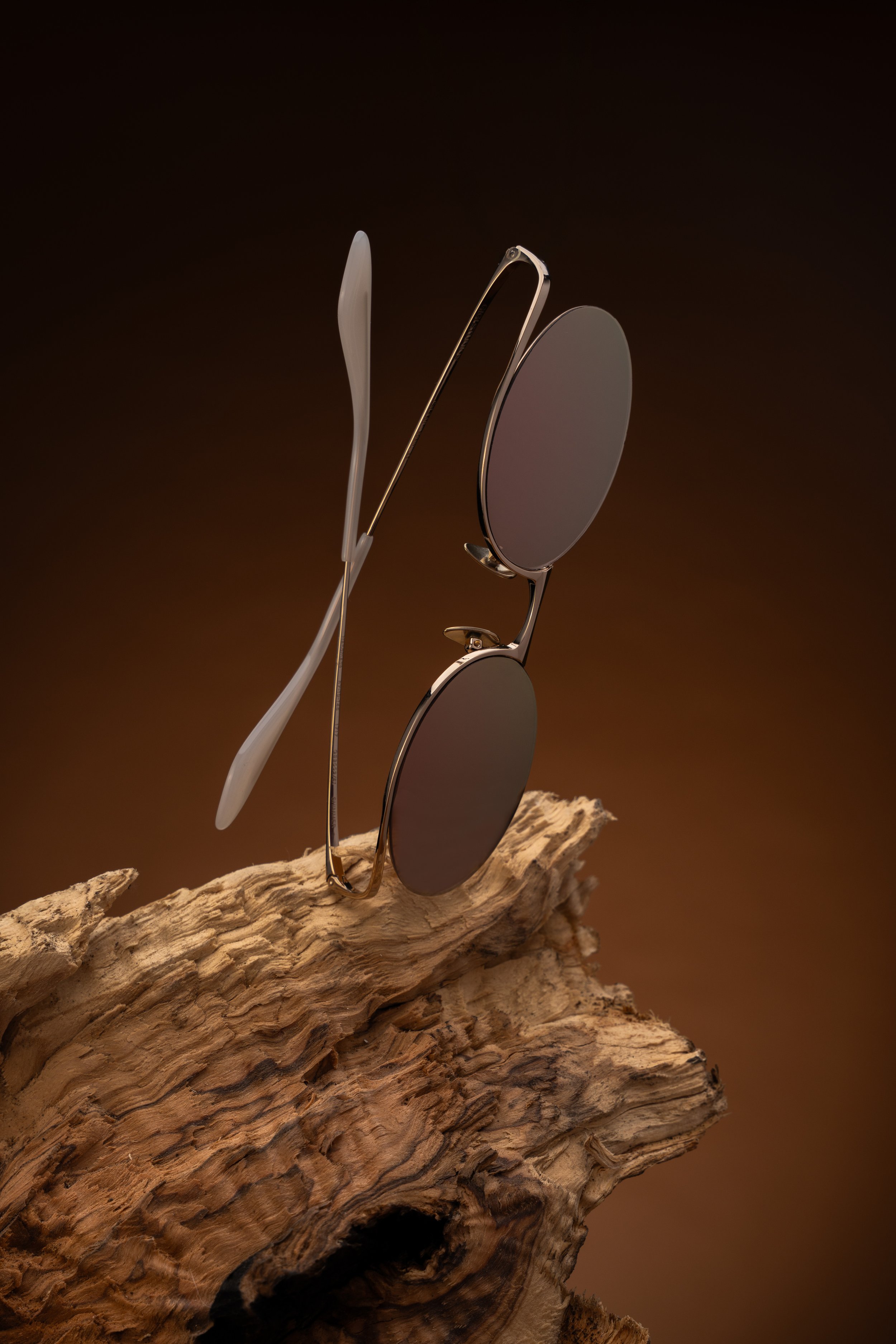 A pair of sunglasses resting on a piece of driftwood against a dark background.