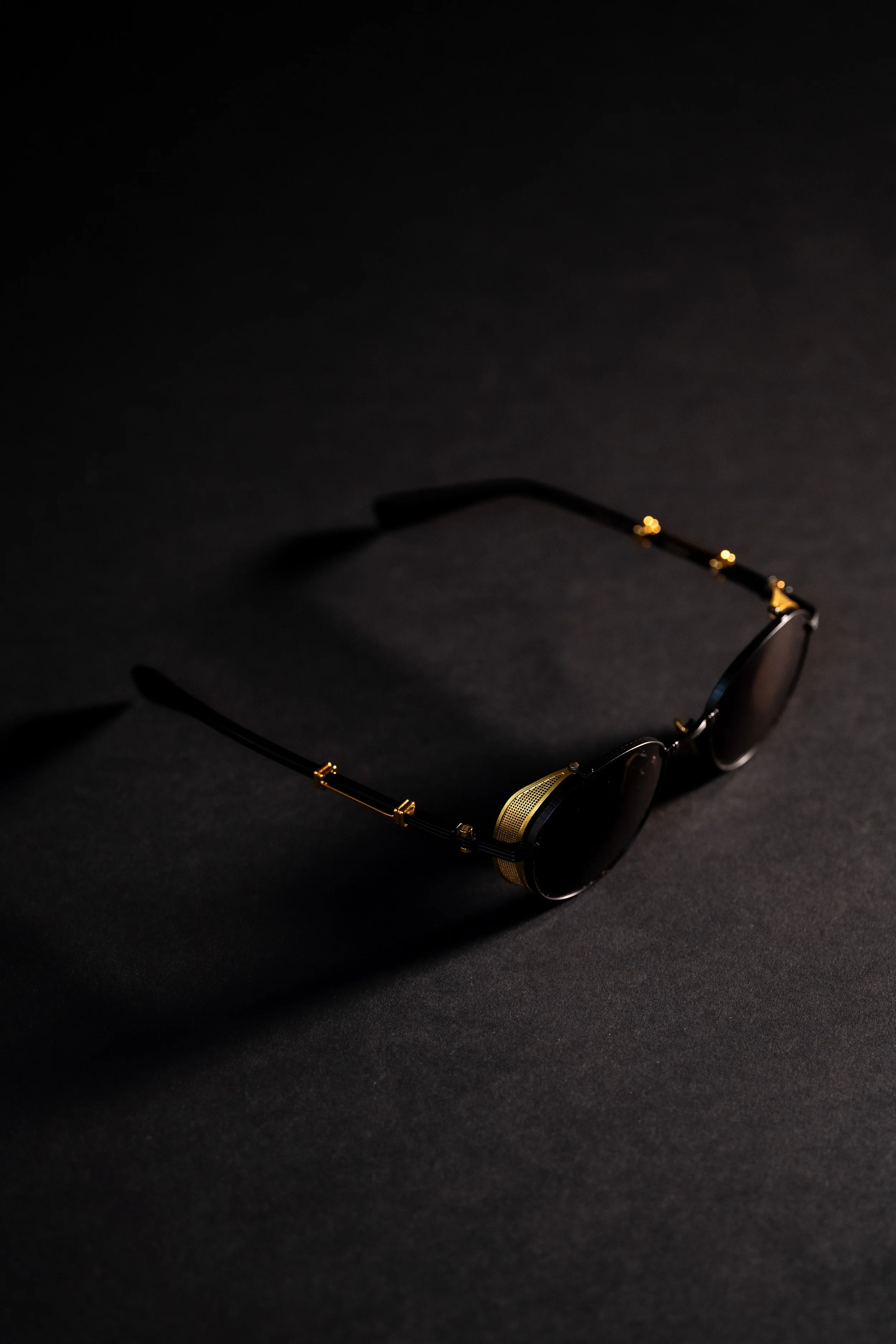 Black sunglasses with gold accents on a dark surface, casting a shadow.