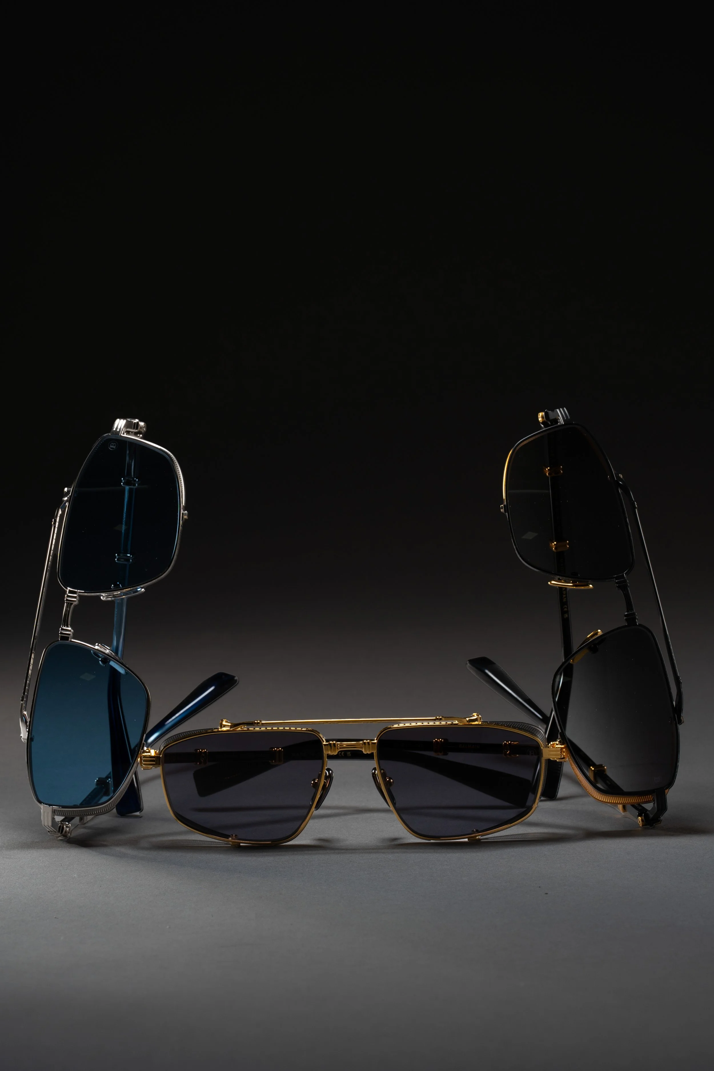 Three pairs of sunglasses, two with black frames and one with a gold frame, displayed on a surface against a dark background.