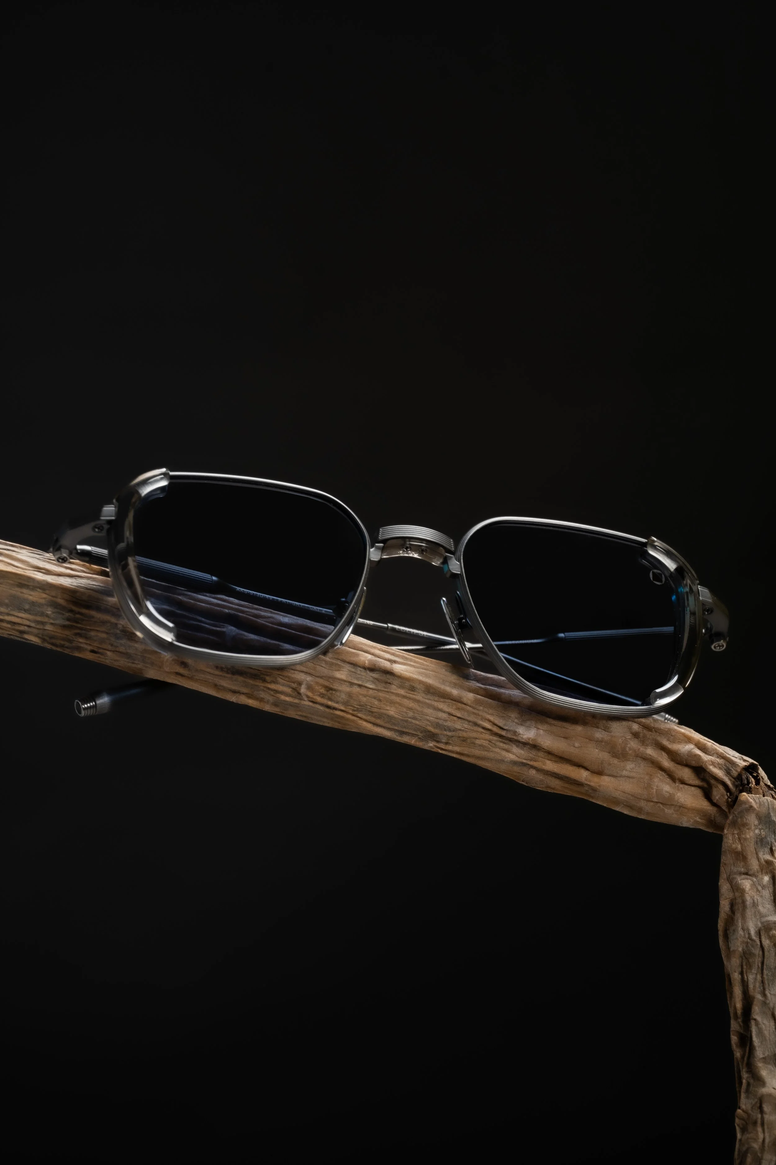 A pair of black sunglasses resting on a piece of weathered wood against a black background.