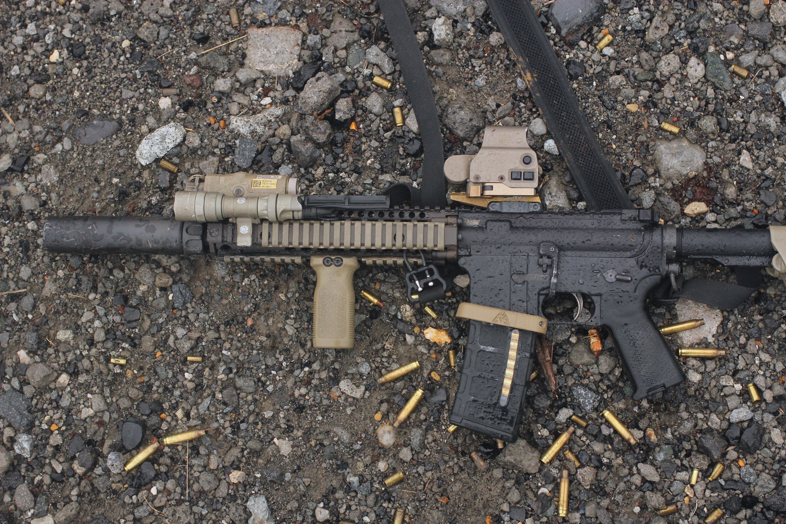 A rifle resting on gravel ground surrounded by spent brass cartridge cases.