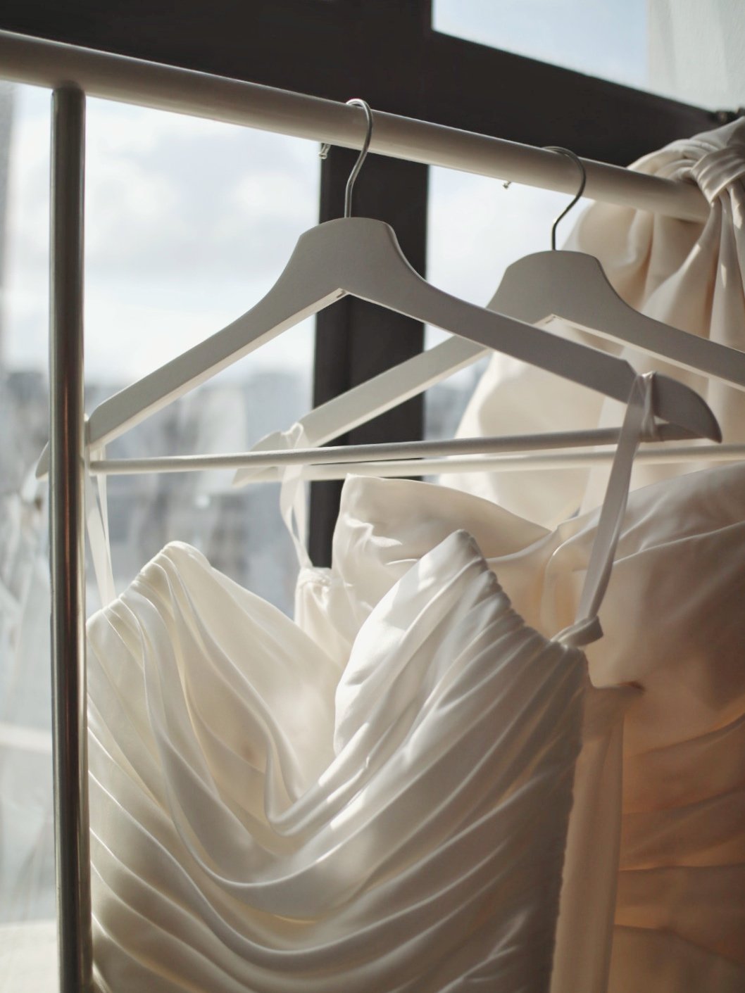 White dresses hanging on a clothing rack near a window.