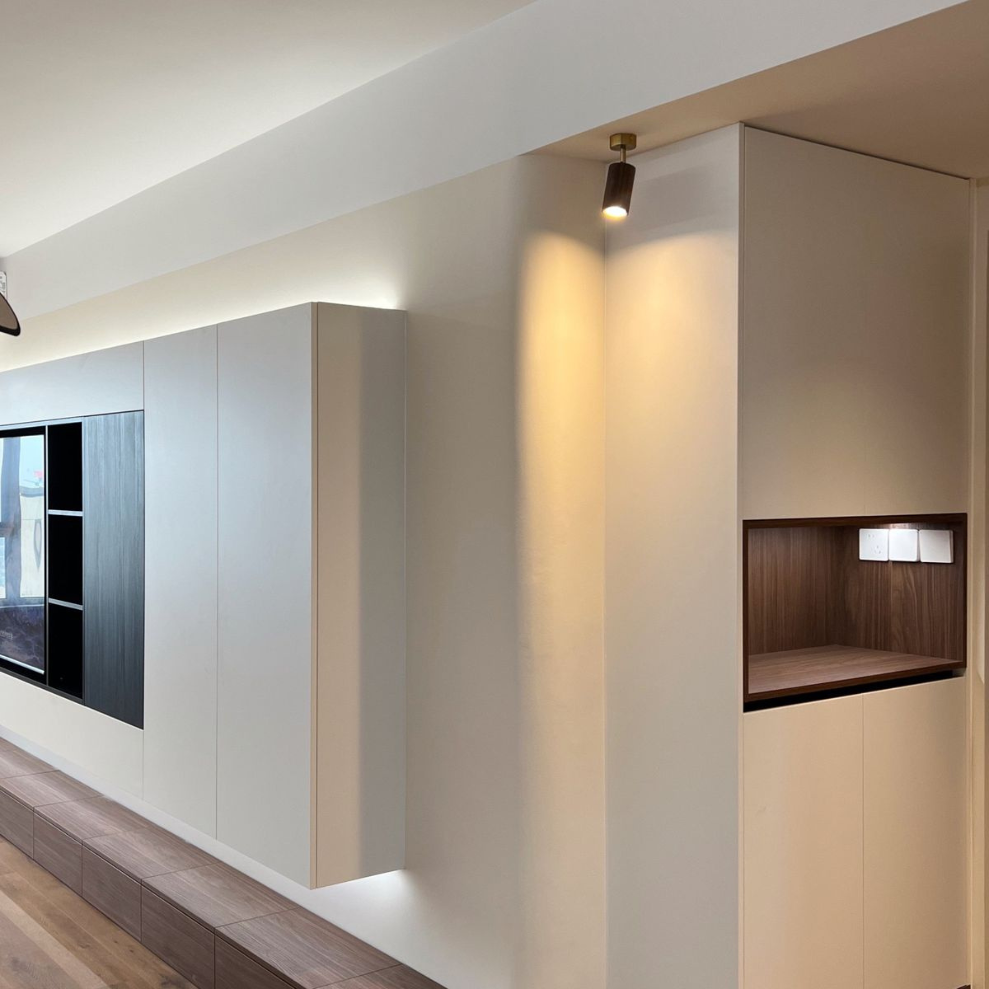 Modern interior wall featuring built-in shelving with electrical outlets, a wood accent, and a spot light above.