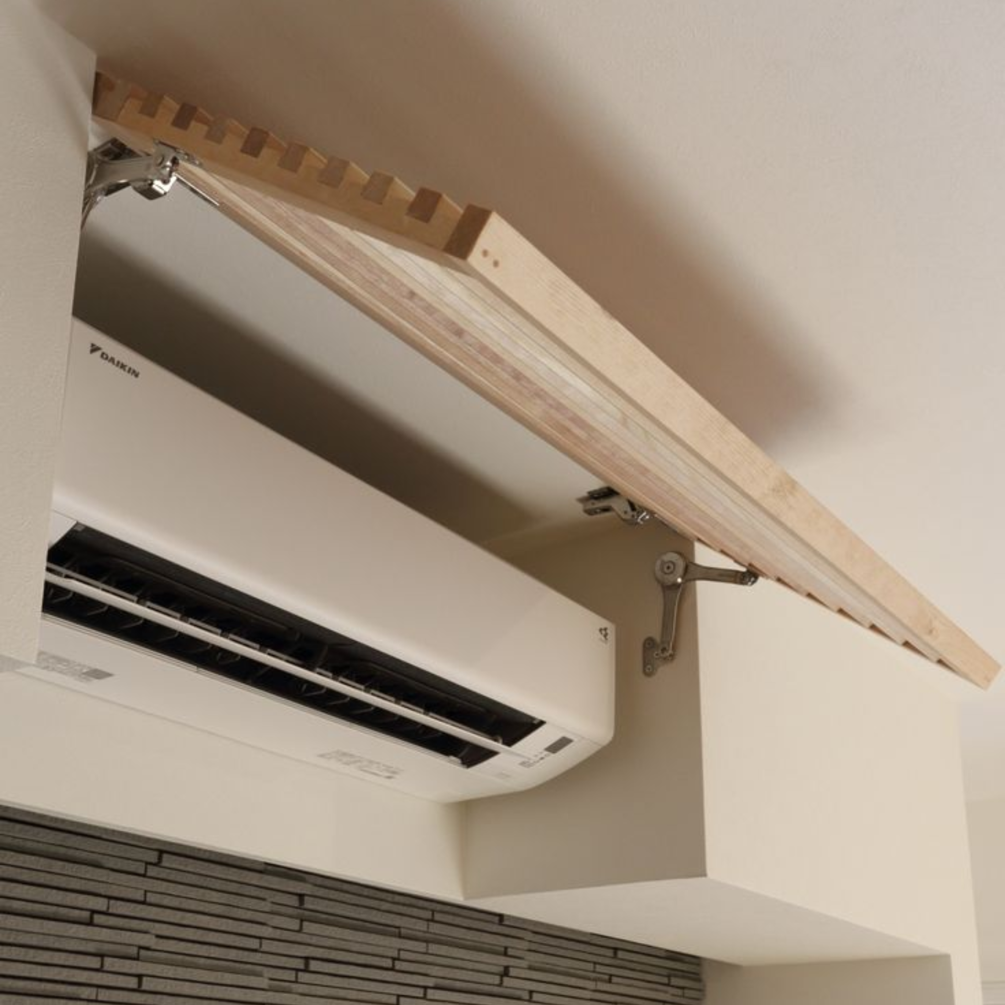 A white Daikin air conditioning unit mounted on the wall underneath a wooden shelf with metal brackets.