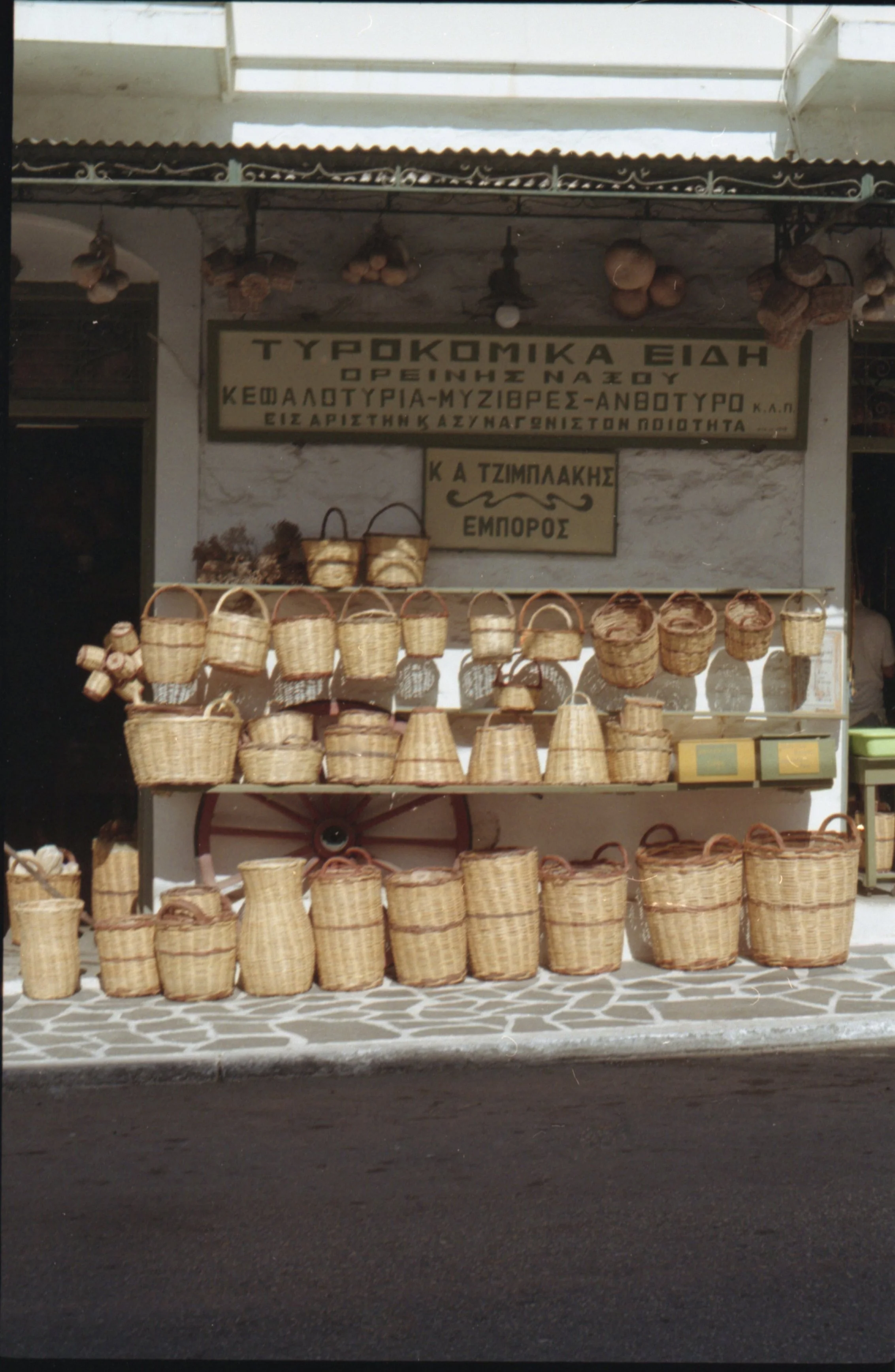 Vitrine d'un magasin de paniers en osier avec des paniers de différentes tailles et formes. Signes en grec au-dessus avec texte mentionnant des produits traditionnels et un nom de vendeur.