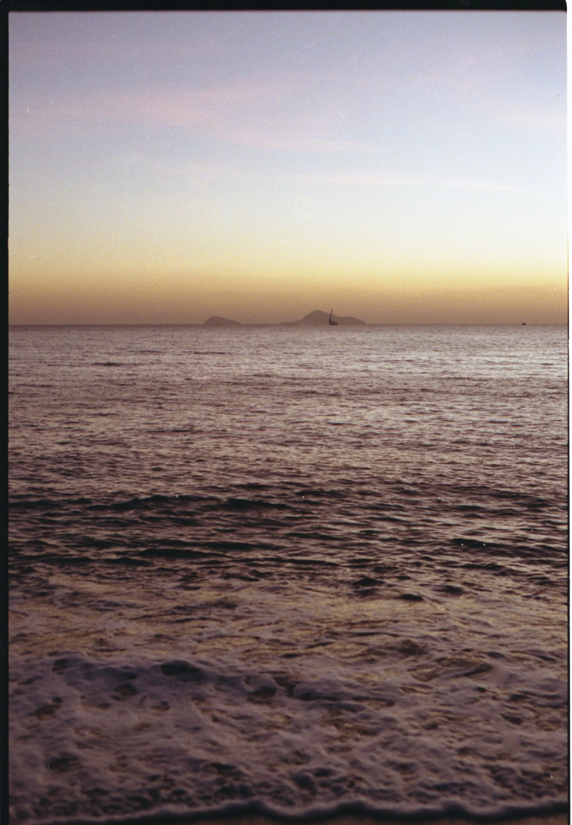 Coucher de soleil sur la mer avec un bateau à voile en arrière-plan, il y a des îles lointaines.