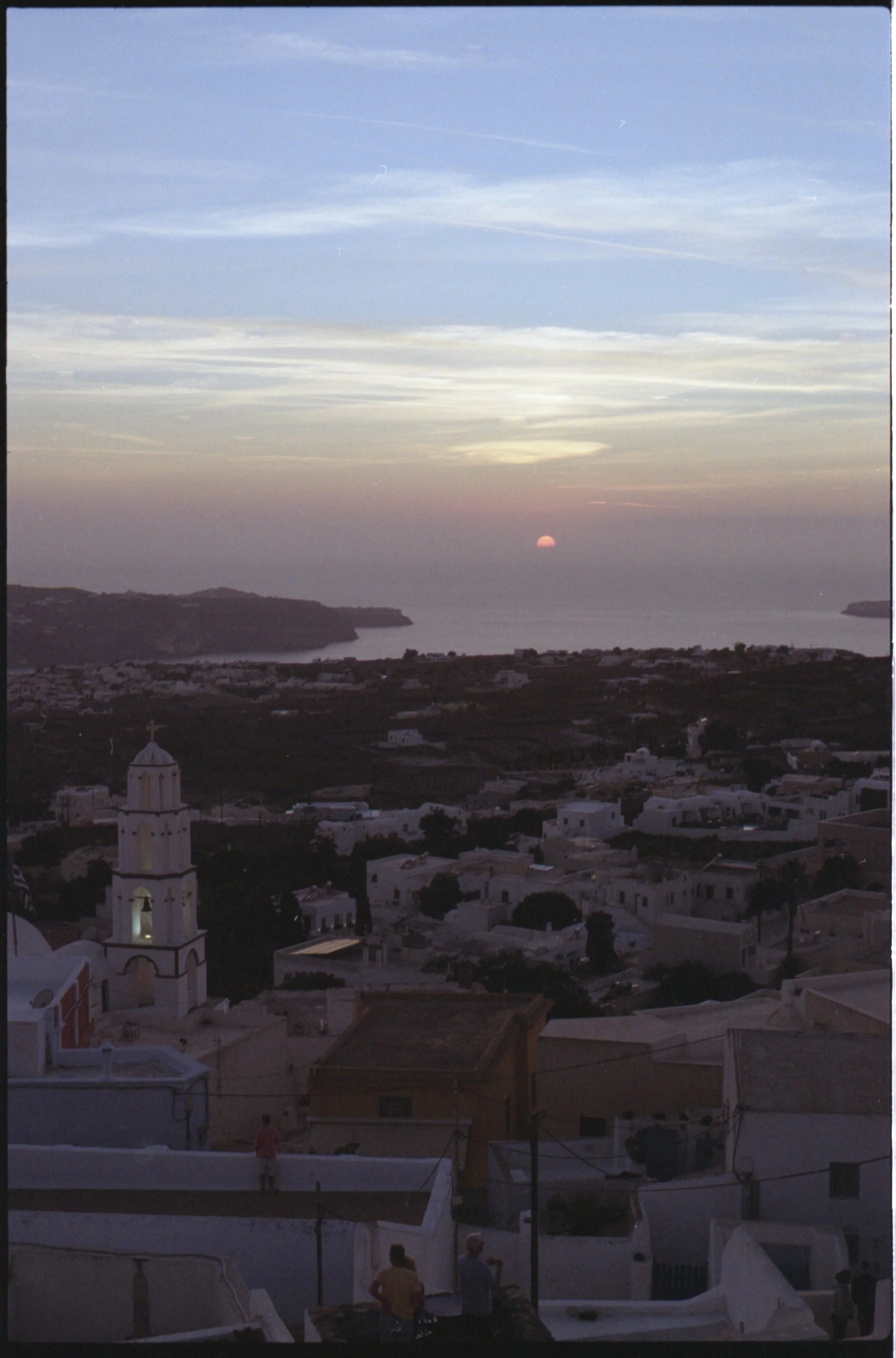 Ciel au coucher du soleil au-dessus d'une ville méditerranéenne avec église blanche, mer et îles environnantes.