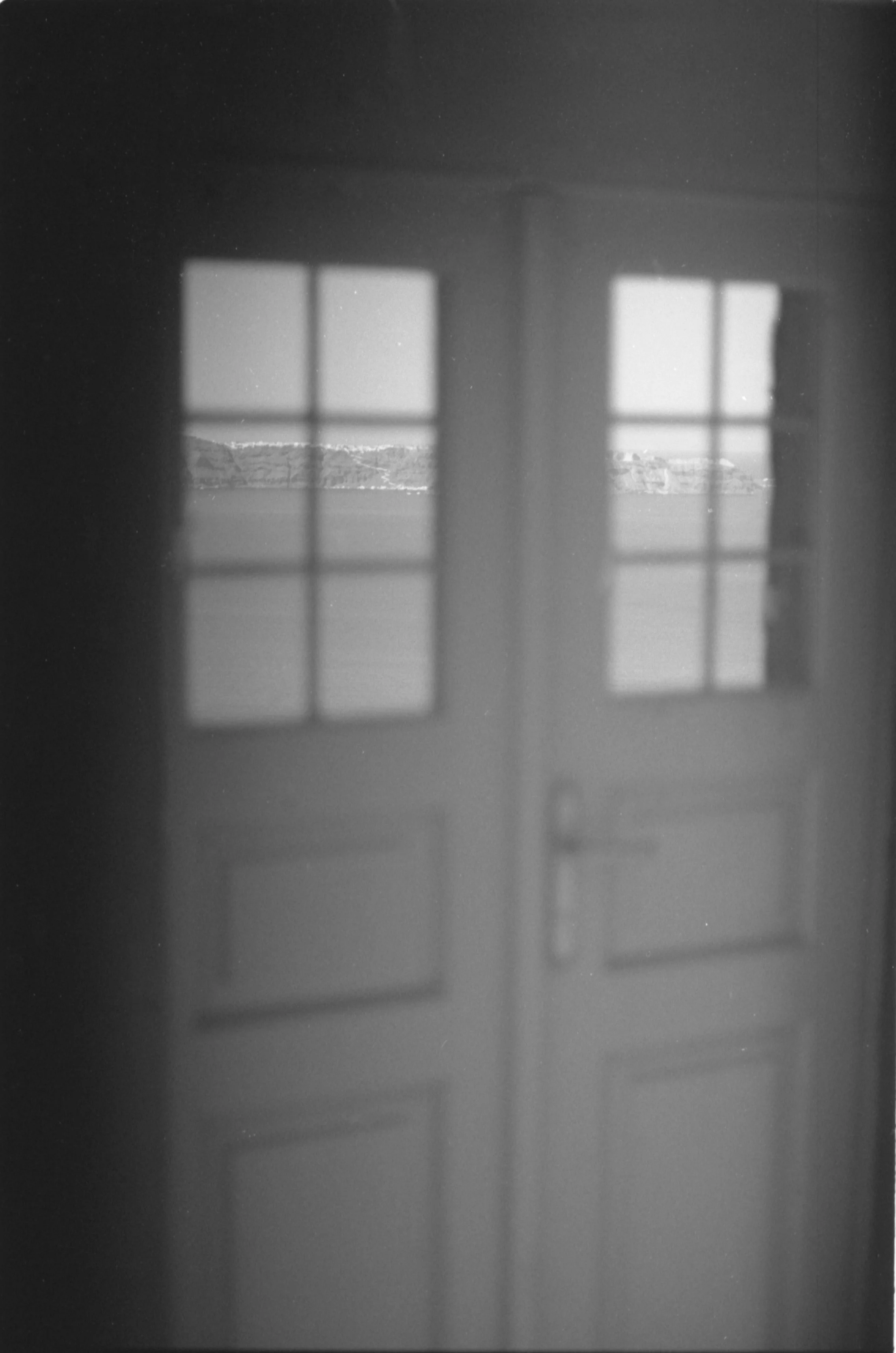 Vue à travers une porte en bois avec des fenêtres en verre, montrant un paysage lointain.