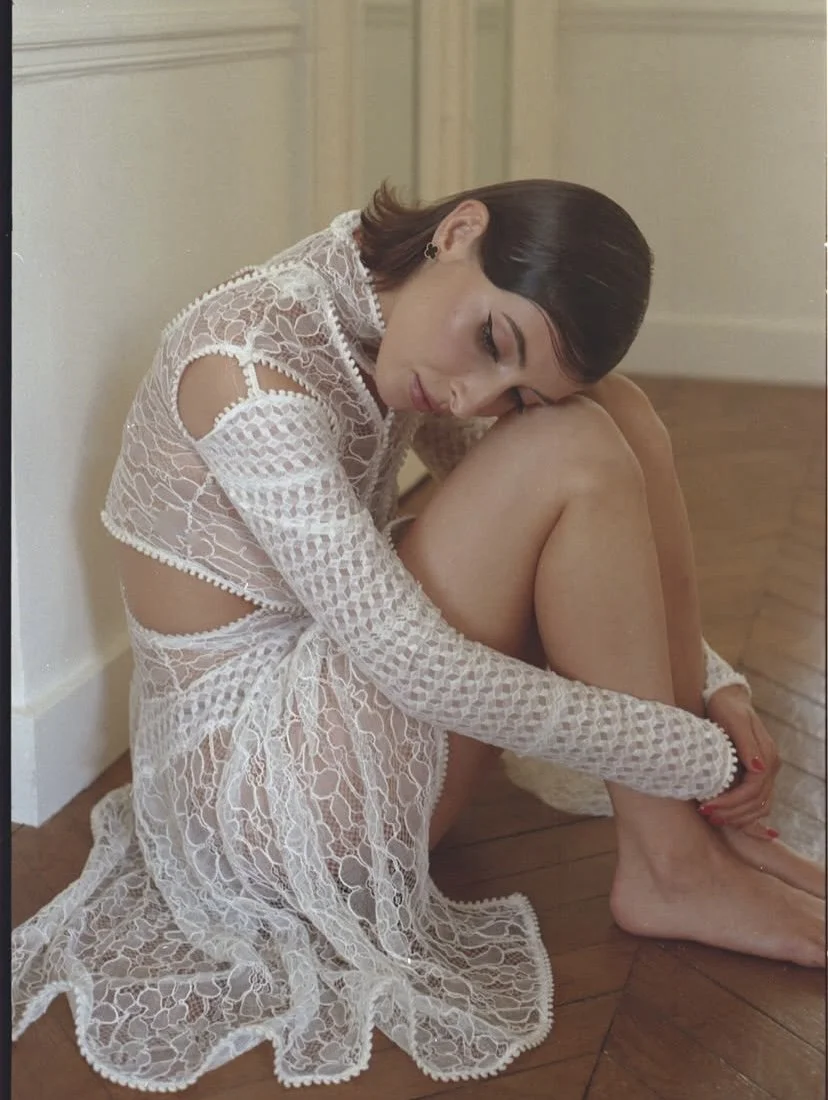 Une femme assise sur le sol en portant une robe en dentelle blanche, pensant ou méditant.