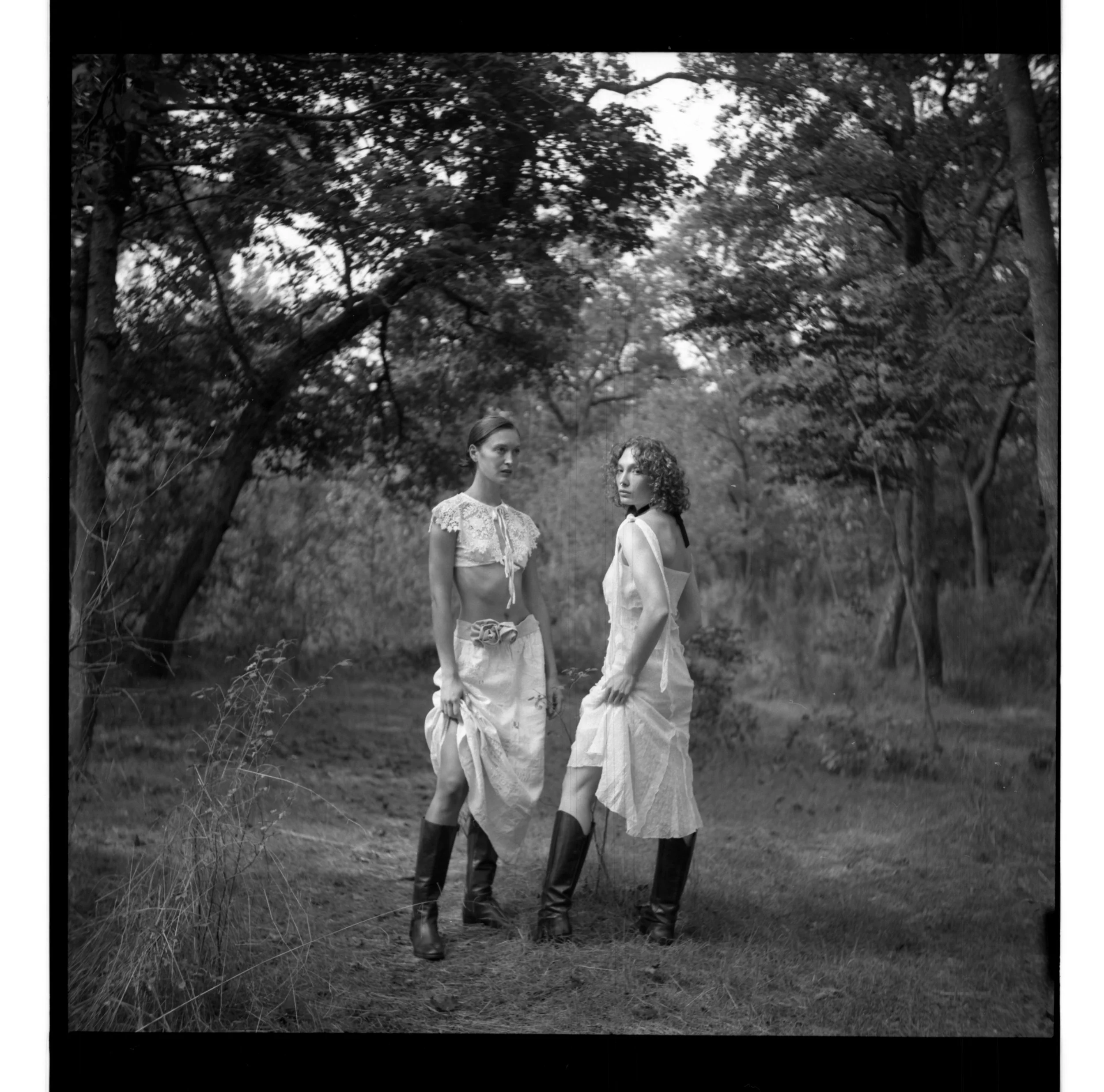 Deux femmes portent des bottes en caoutchouc et des robes longues dans une forêt, en noir et blanc.