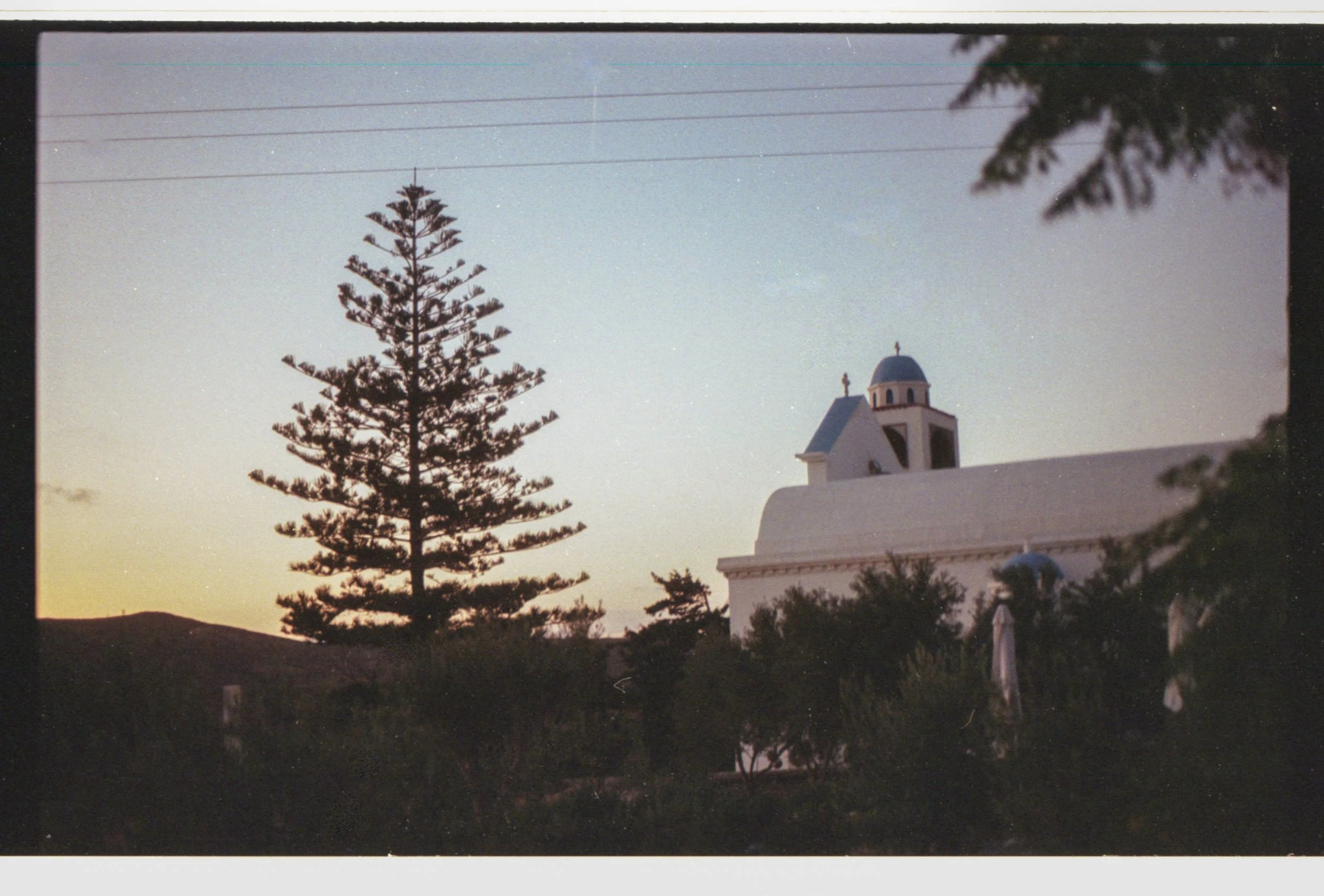 Église blanche avec un dôme bleu, arbres et ciel au coucher du soleil
