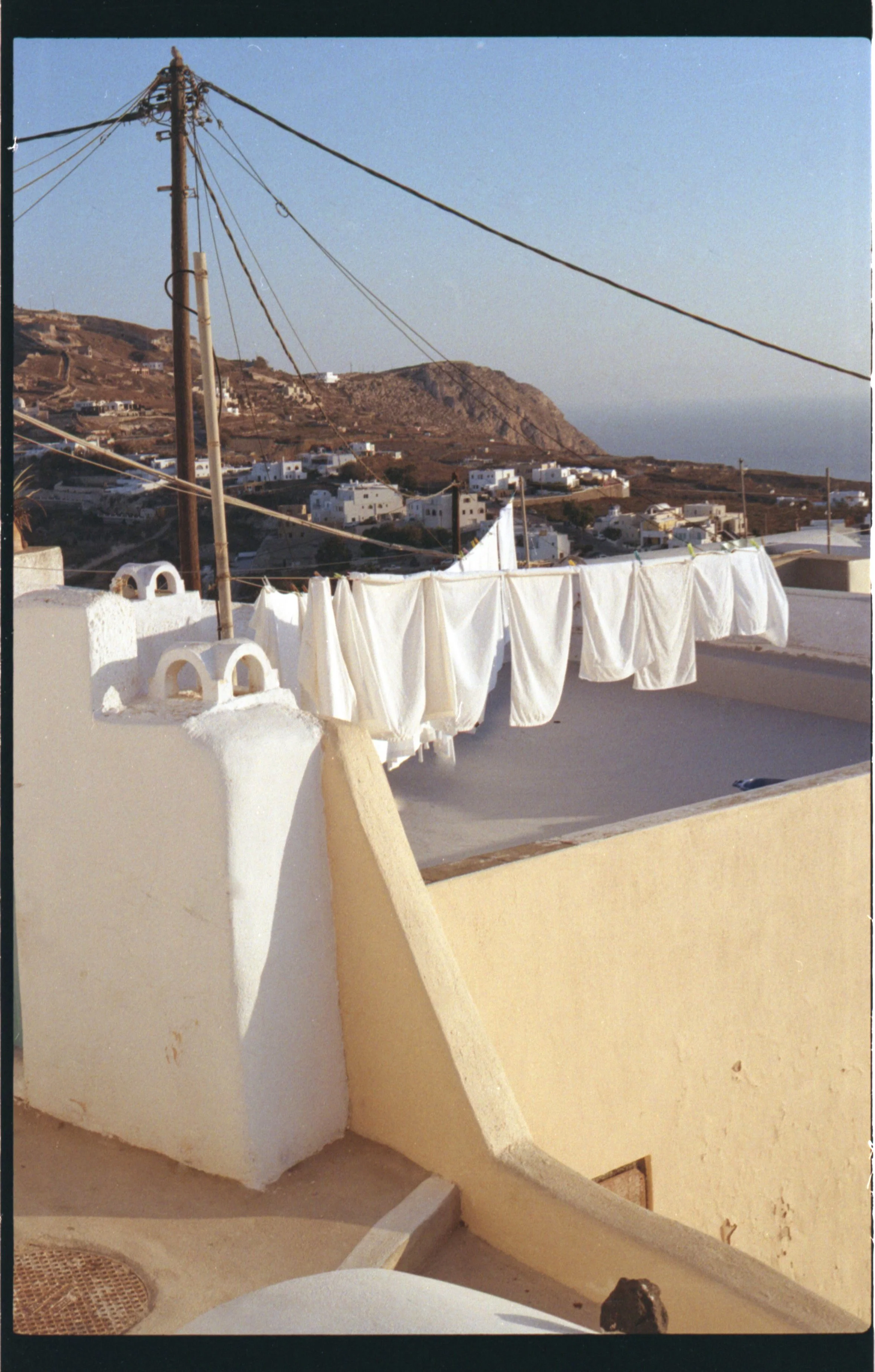 Lavage du linge blanc suspendu sur une corde à linge dans un paysage méditerranéen avec maisons blanches et collines en arrière-plan.
