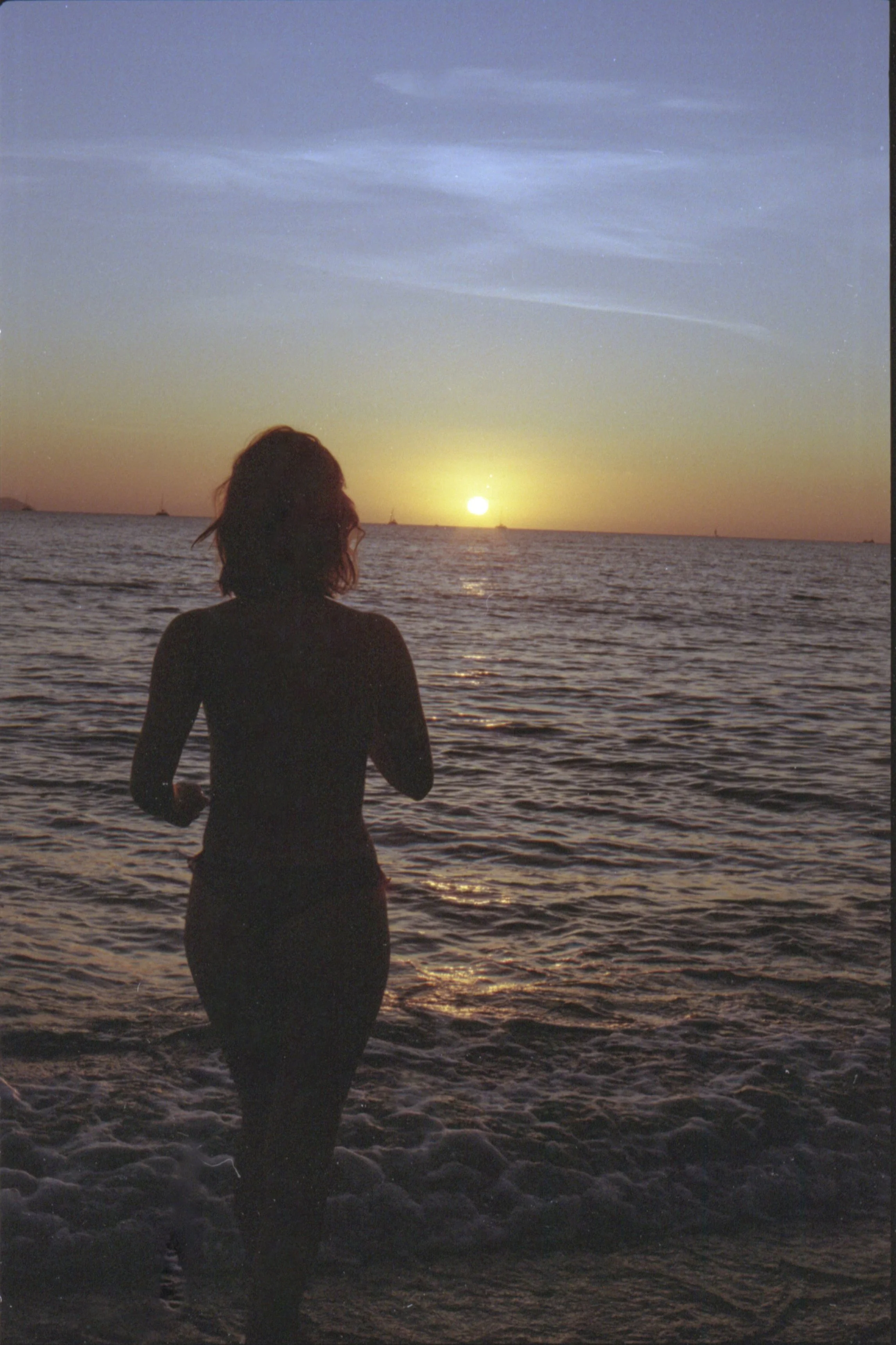Silhouette d'une femme entrant dans la mer au coucher du soleil, avec un ciel coloré en arrière-plan.