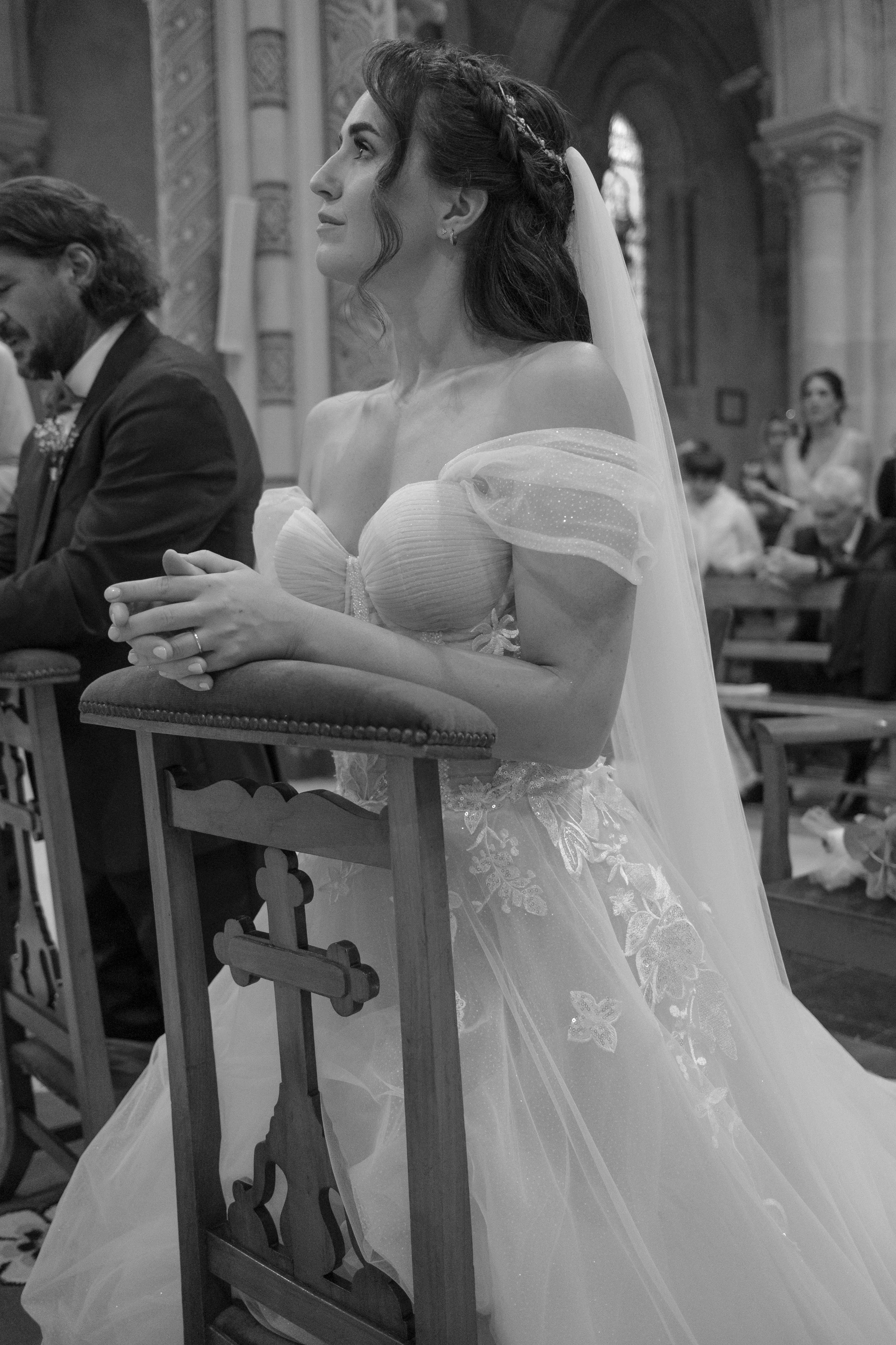 Une femme lors d'une cérémonie religieuse, probablement un mariage, en prière ou en méditation, dans une église, vêtue d'une robe de mariée avec voile.