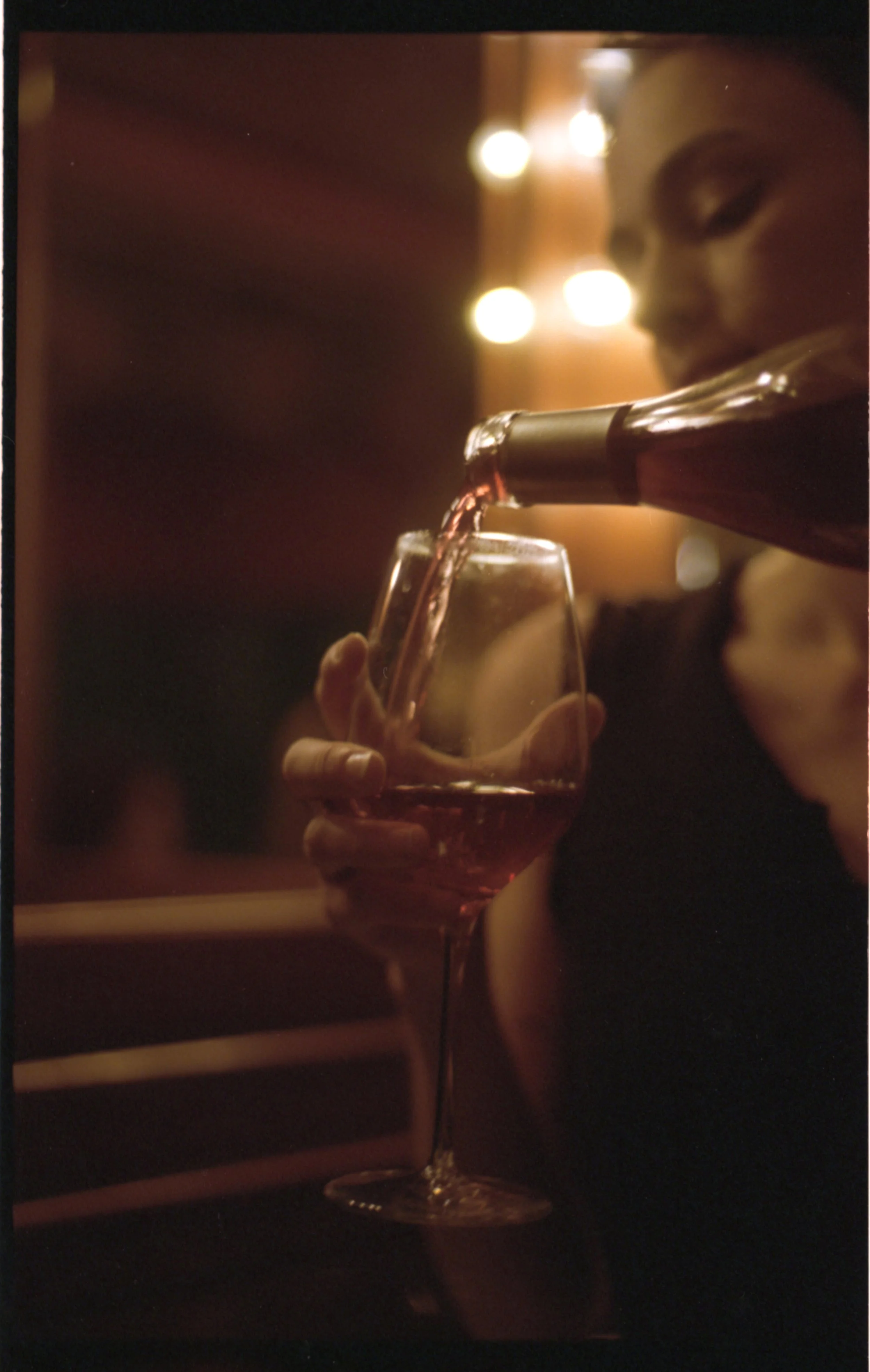 Une personne verse du vin rosé dans un verre à vin, avec une lumière chaleureuse en arrière-plan.