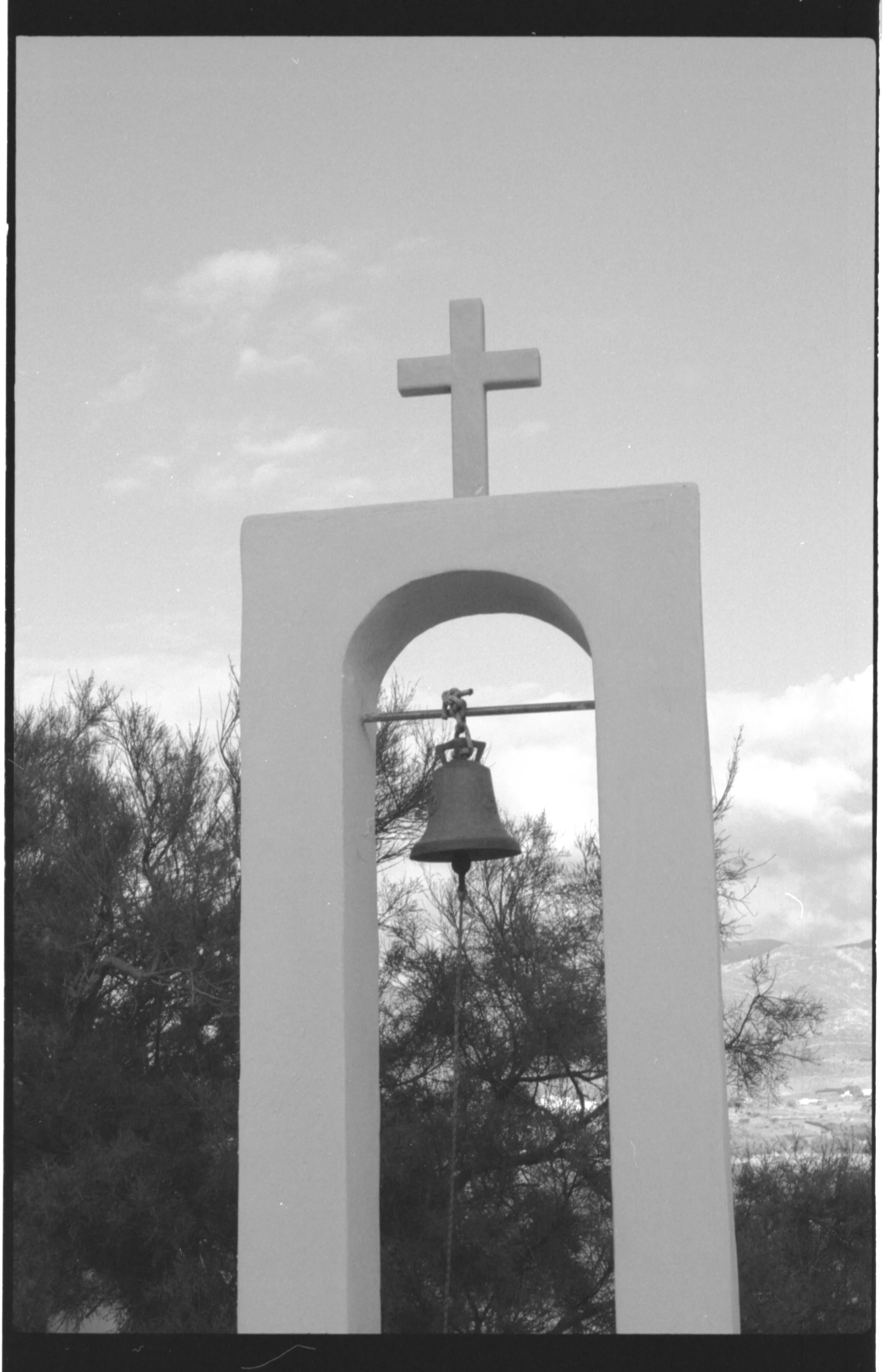 Cloche de chœur avec une croix en haut, dans un paysage naturel avec des arbres et un ciel nuageux