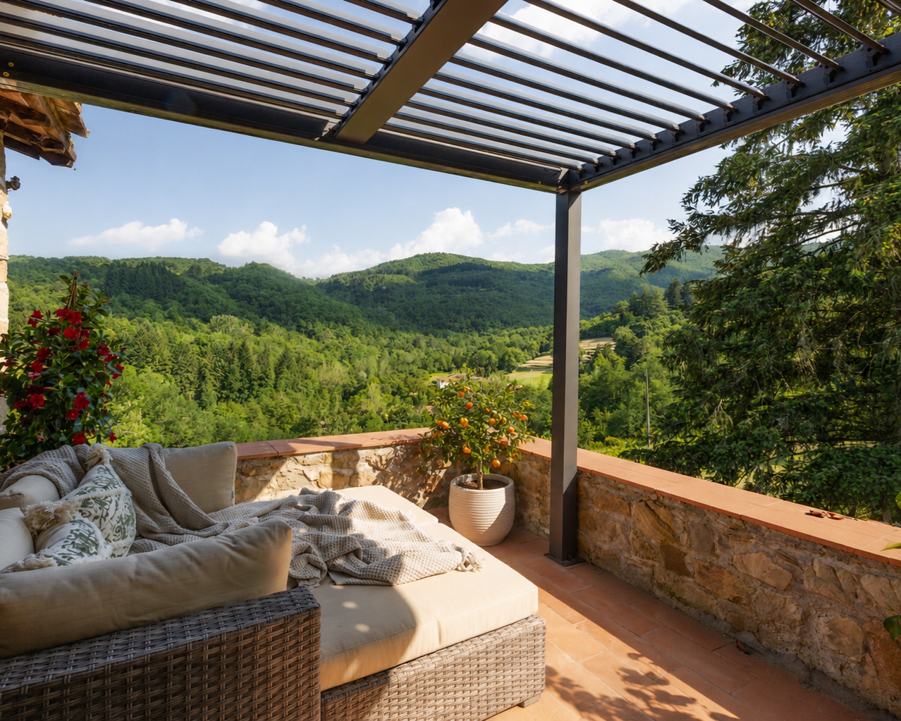 Outdoor patio with wicker couch and cushions, potted orange tree, and lush green hills in the background under a blue sky with scattered clouds.