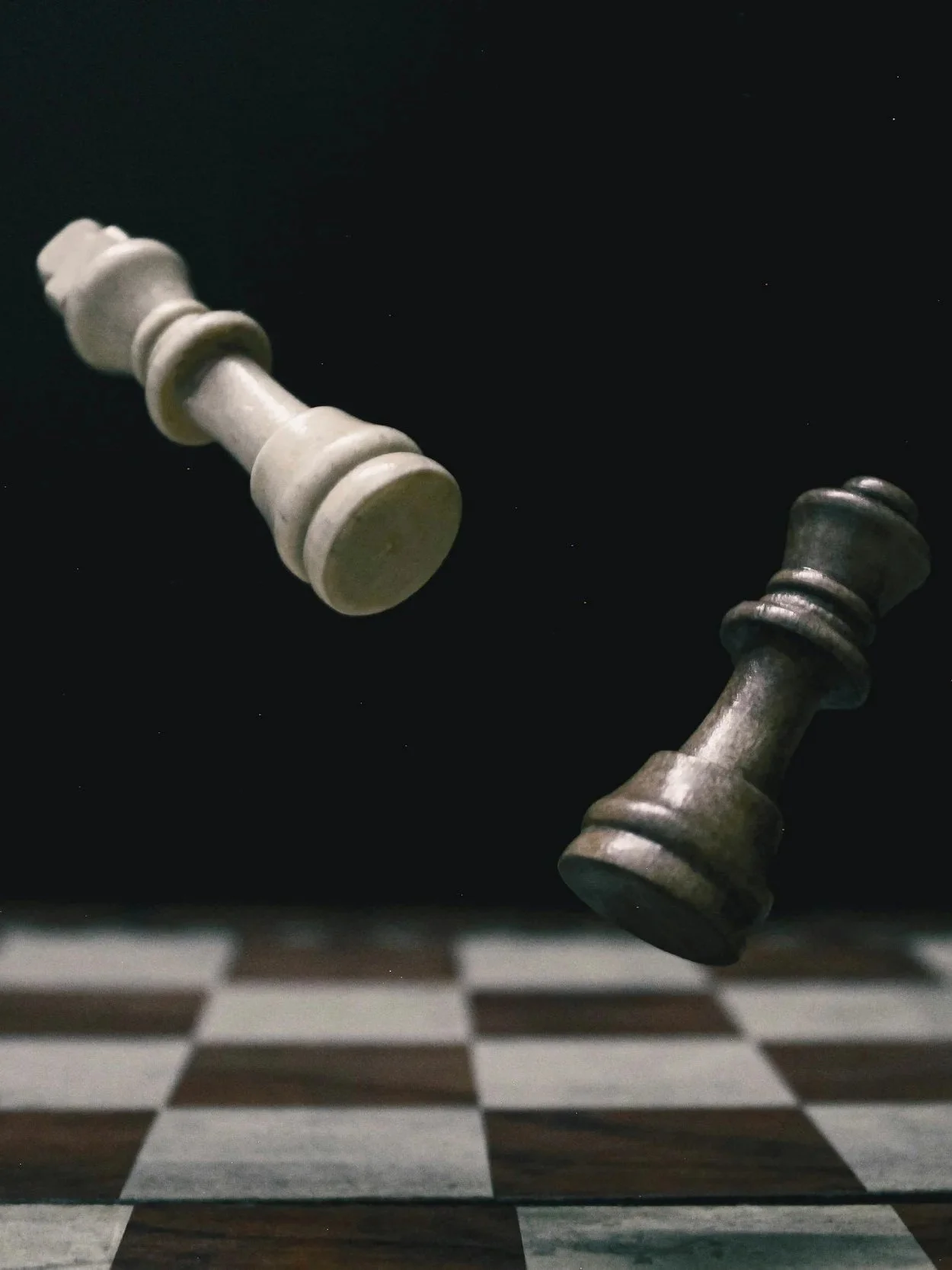 Two chess kings falling onto a chessboard with dark background