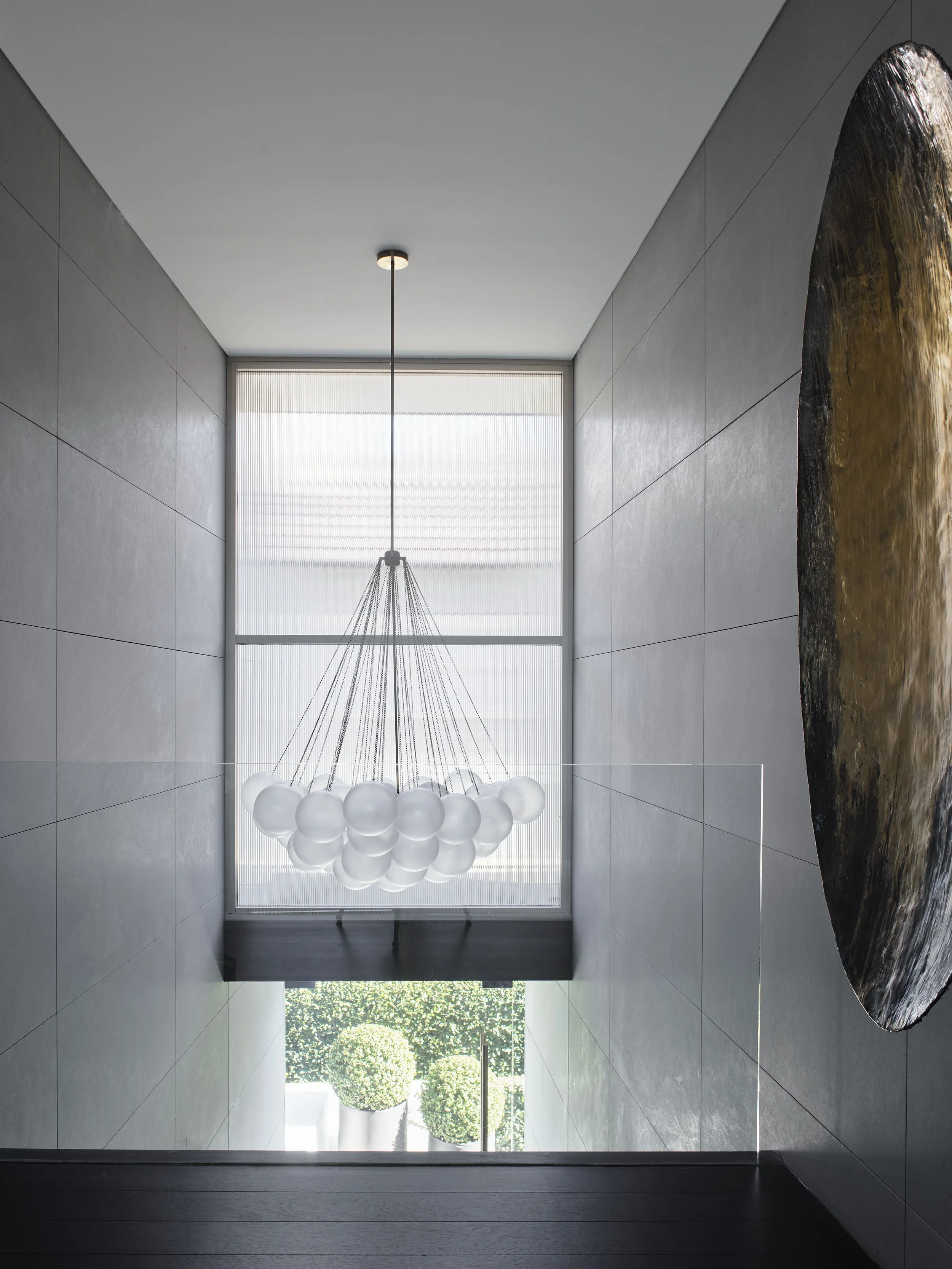 Modern hallway with a chandelier near large window and a rock sculpture on the right wall.
