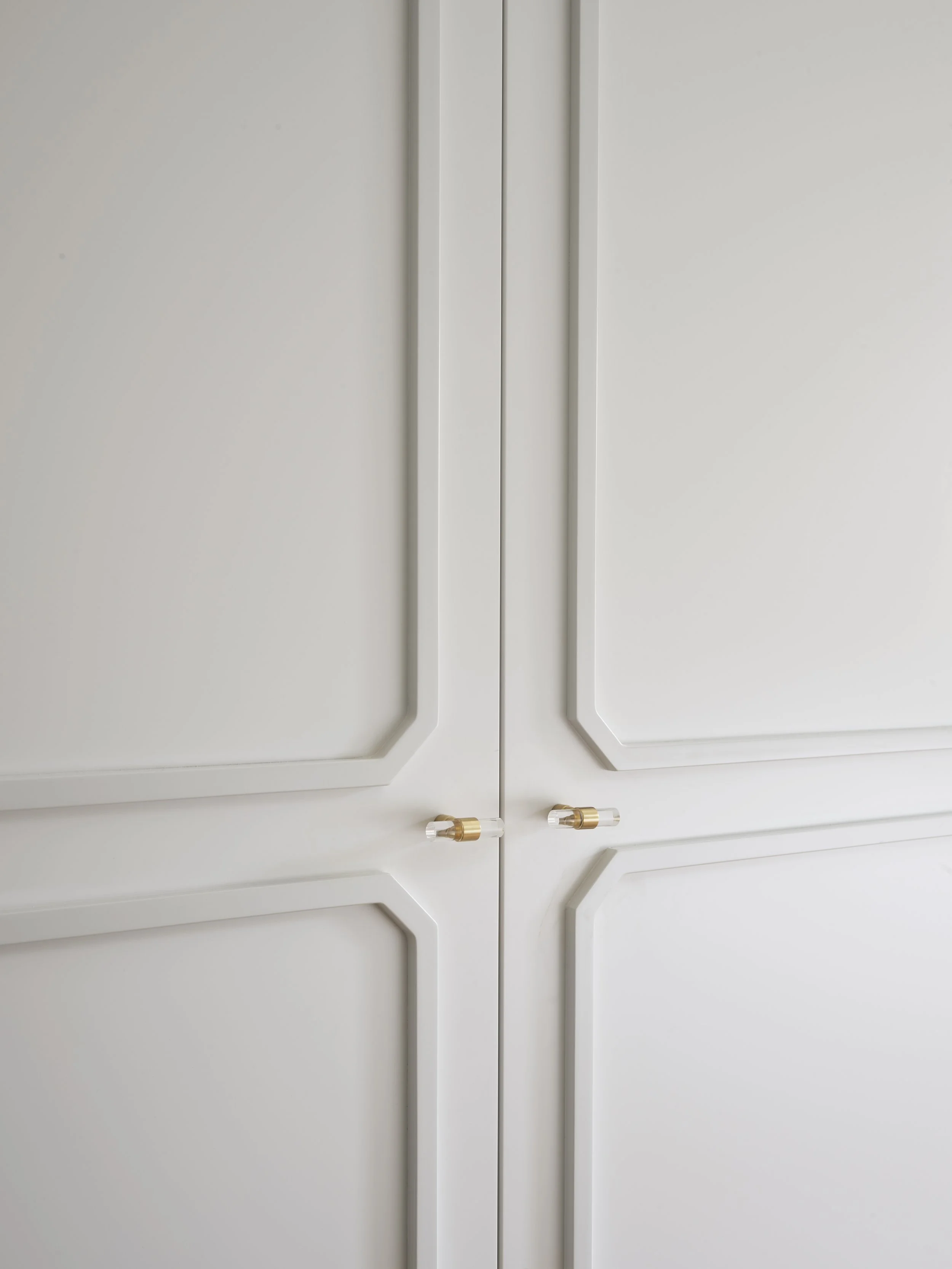 Close-up of white closet or cabinet doors with gold and clear knobs.