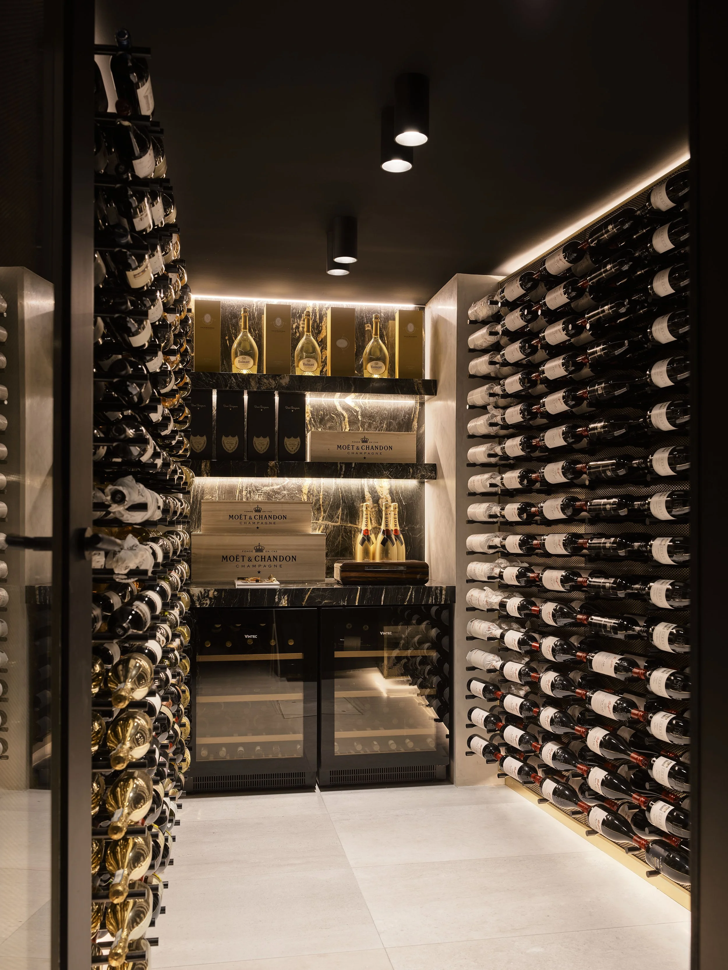 A luxurious wine cellar with wine bottles stored on racks along the walls, a small refrigerator, and decorative champagne bottles on the shelves in the back.
