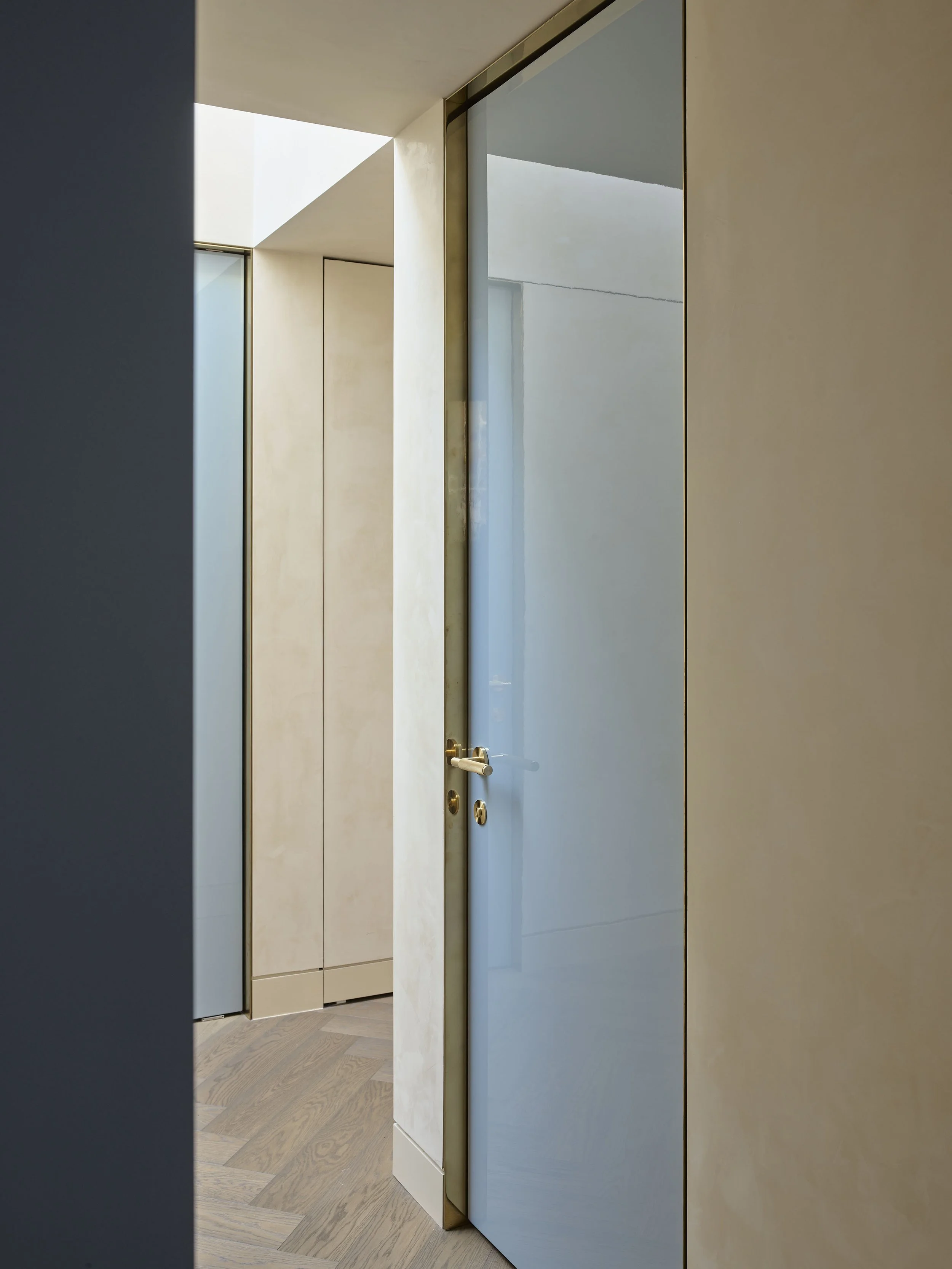 Modern interior hallway with beige walls, wooden flooring, and large glass doors with gold trim.