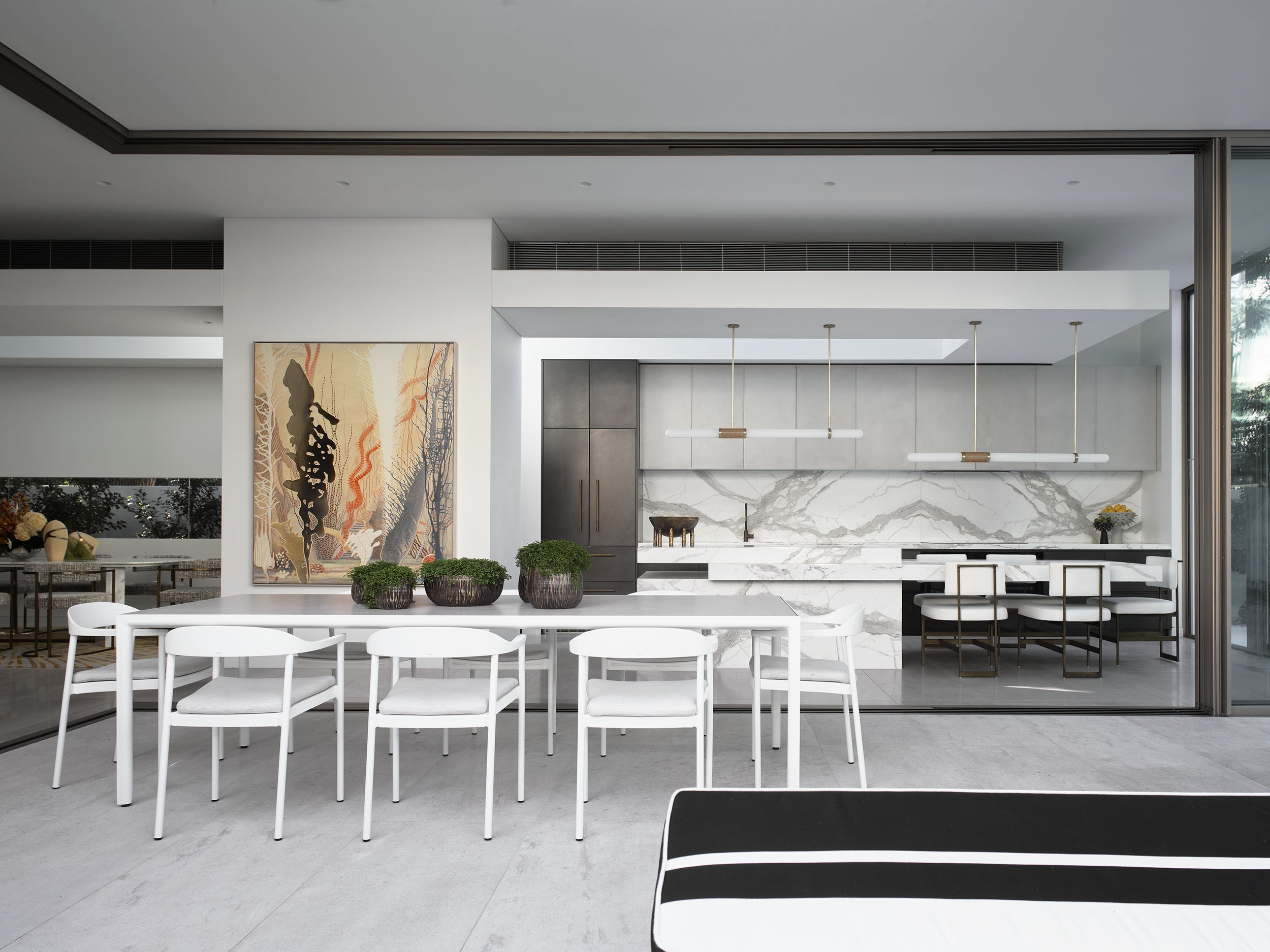Modern interior with white dining table, white chairs, and a kitchen featuring marble backsplash, gray cabinets, and pendant lighting.