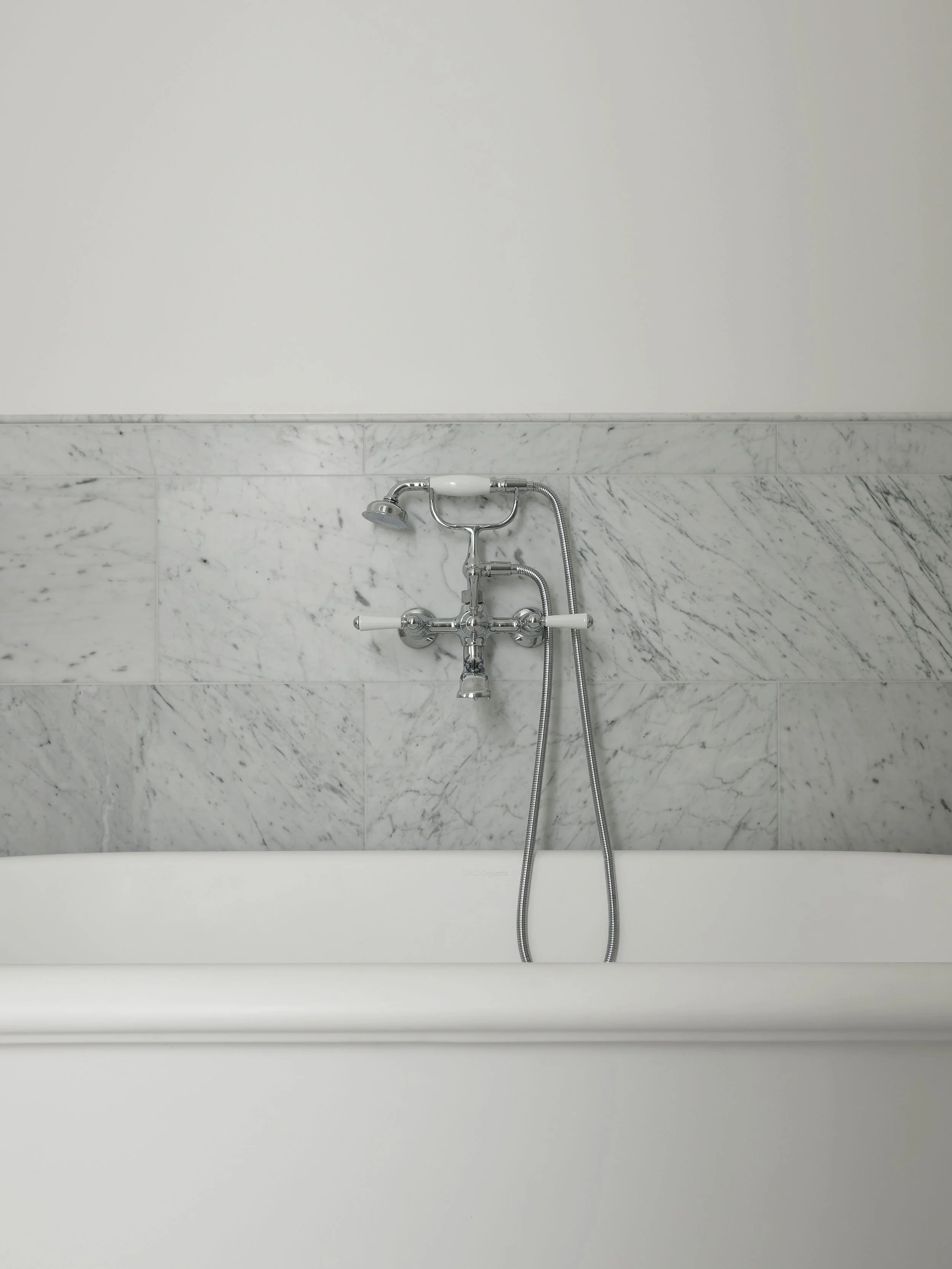 Close-up of a bathtub faucet and handheld shower head mounted on a marble wall in a bathroom.
