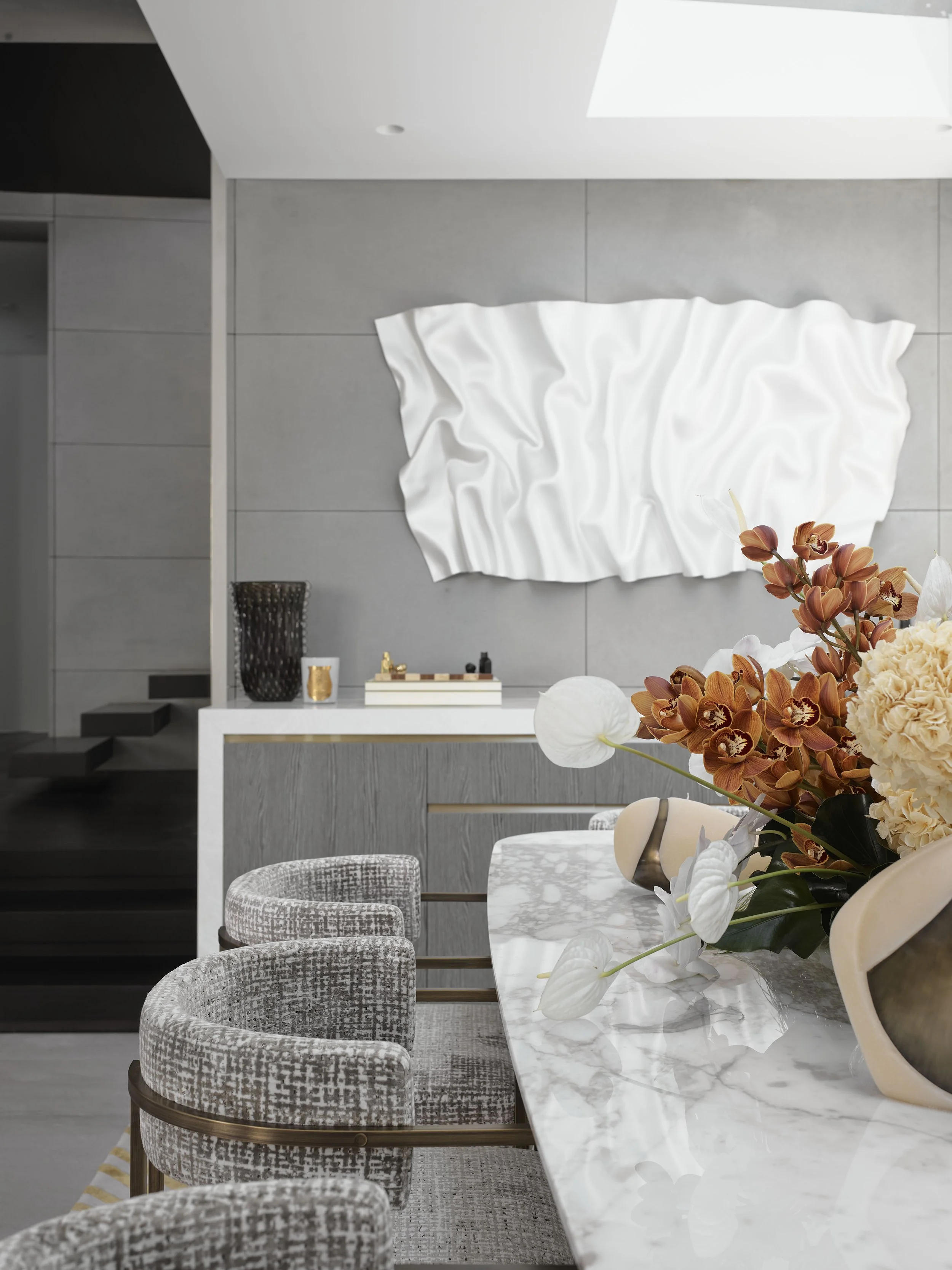 Modern dining room with a marble table, floral centerpiece, textured chairs, and artwork on the wall.
