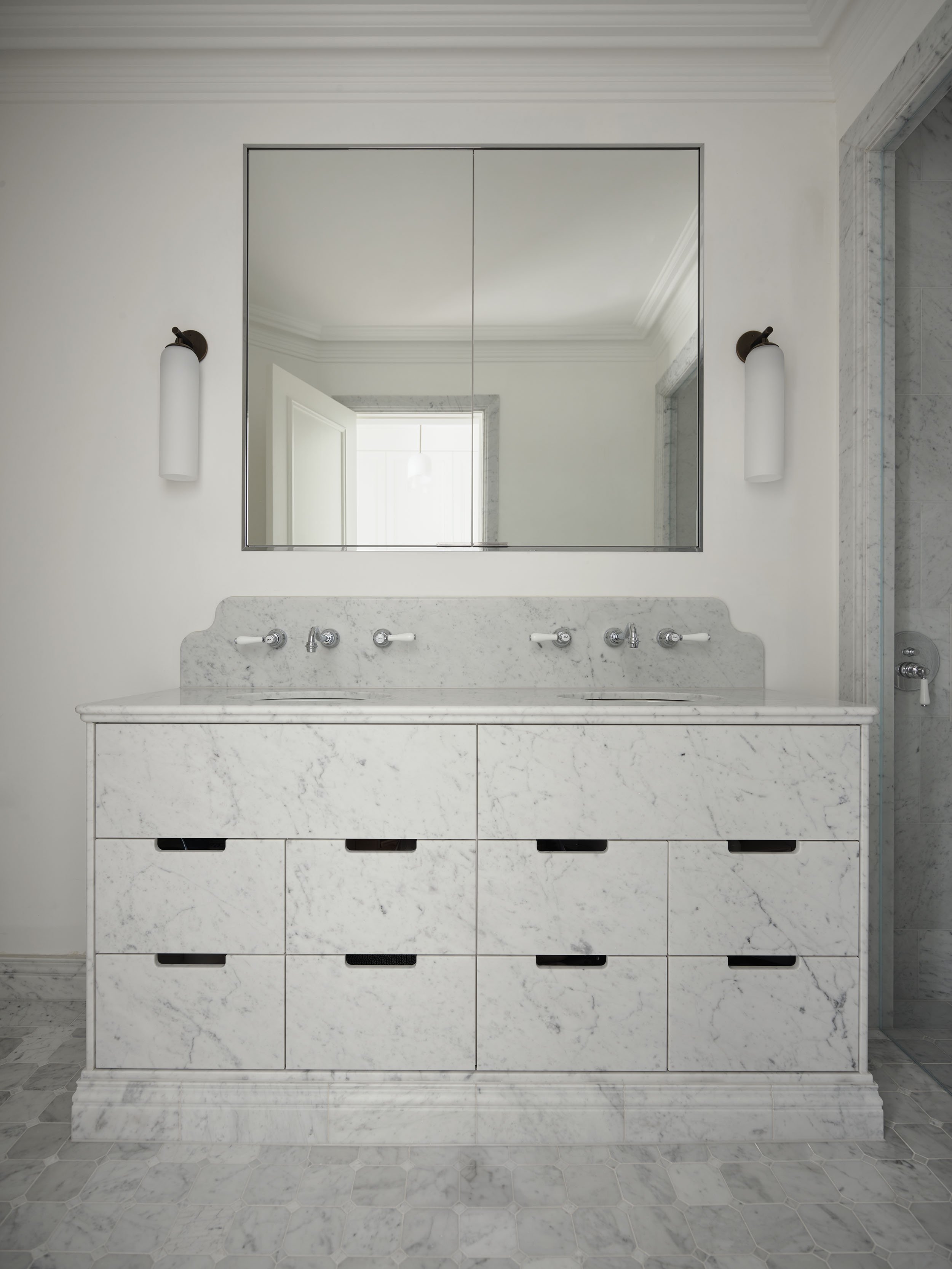 Bathroom vanity with marble countertop and a large mirror above, flanked by wall-mounted light fixtures.