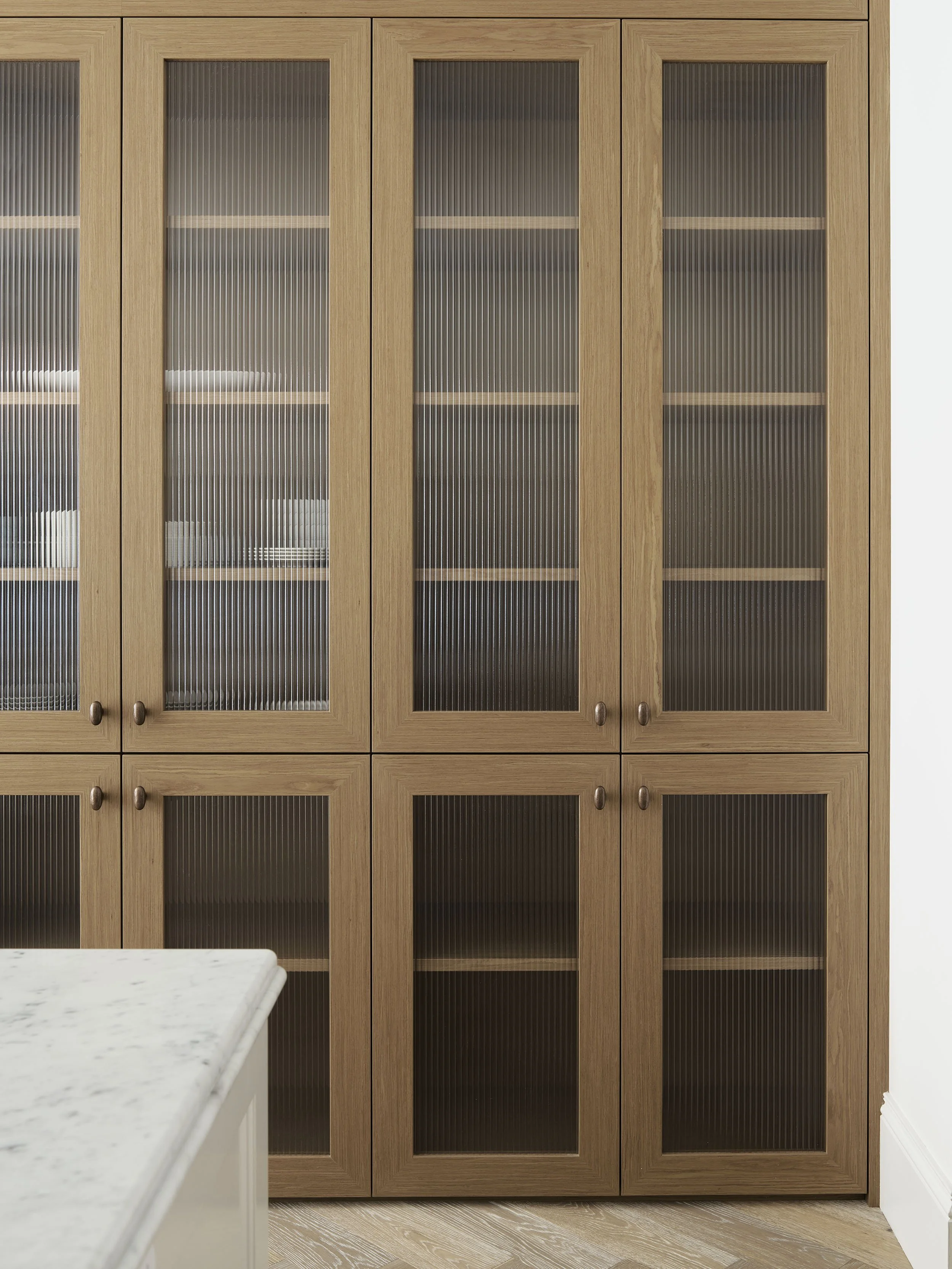 A wooden kitchen cabinet with glass doors and shelves, partially reflecting the room's interior.