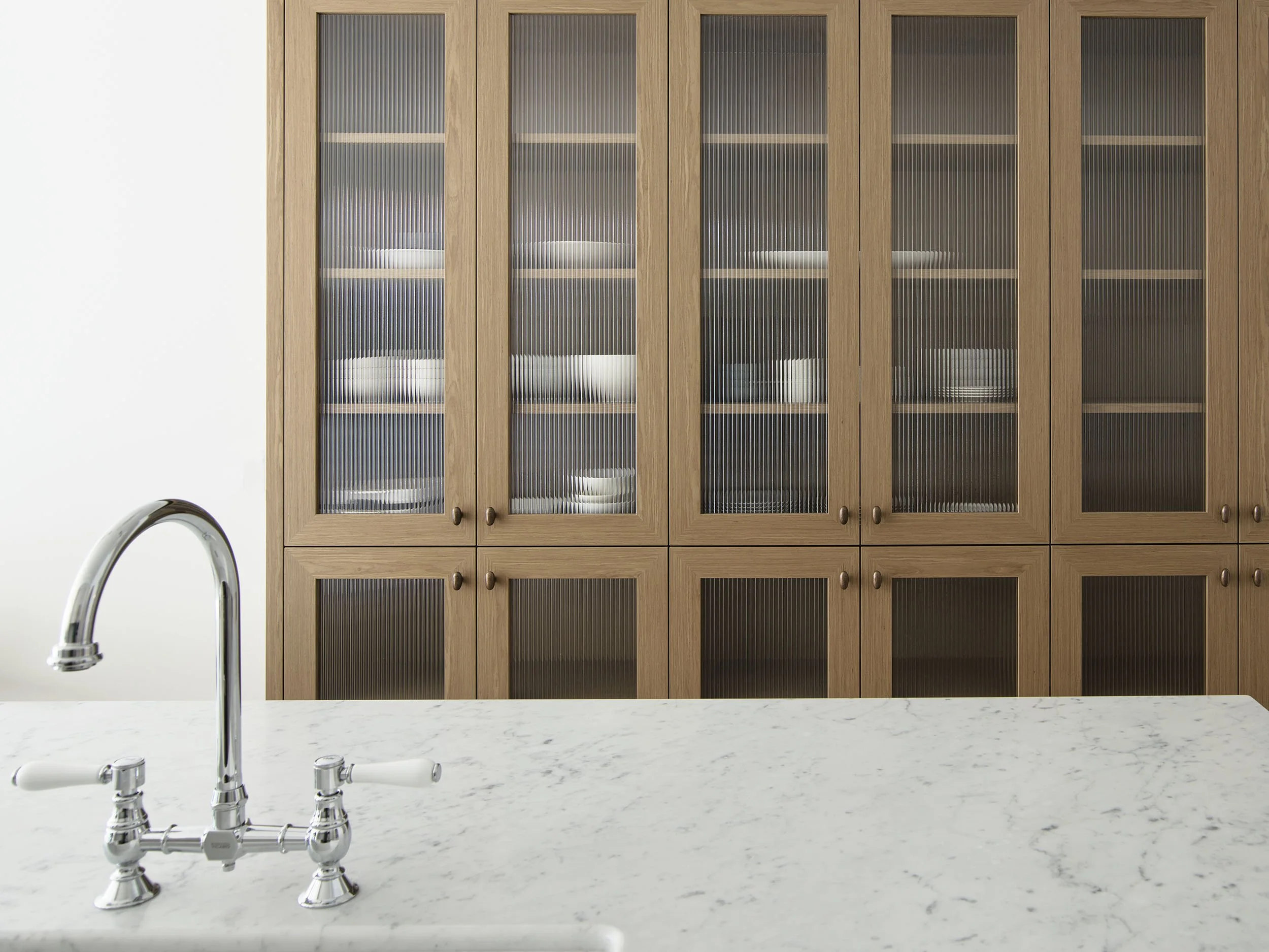 Kitchen with wood cabinet filled with plates and bowls, marble countertop, and a chrome faucet.